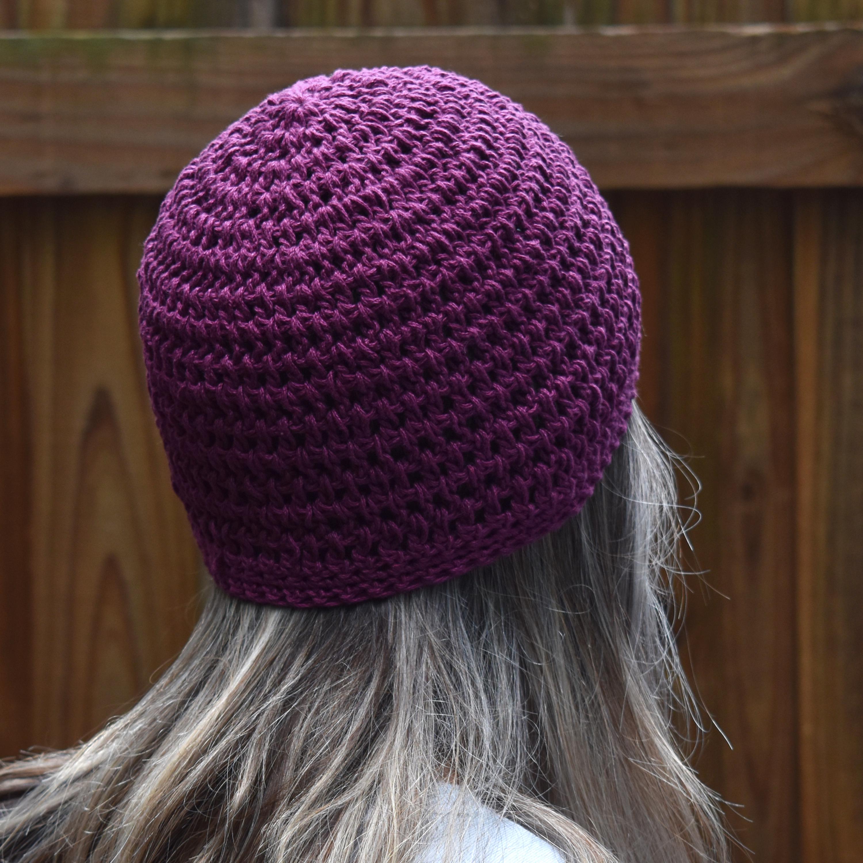 Person wearing a purple knitted beanie with a wooden fence background.