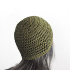 Green knitted beanie on a person with gray hair against a white background.