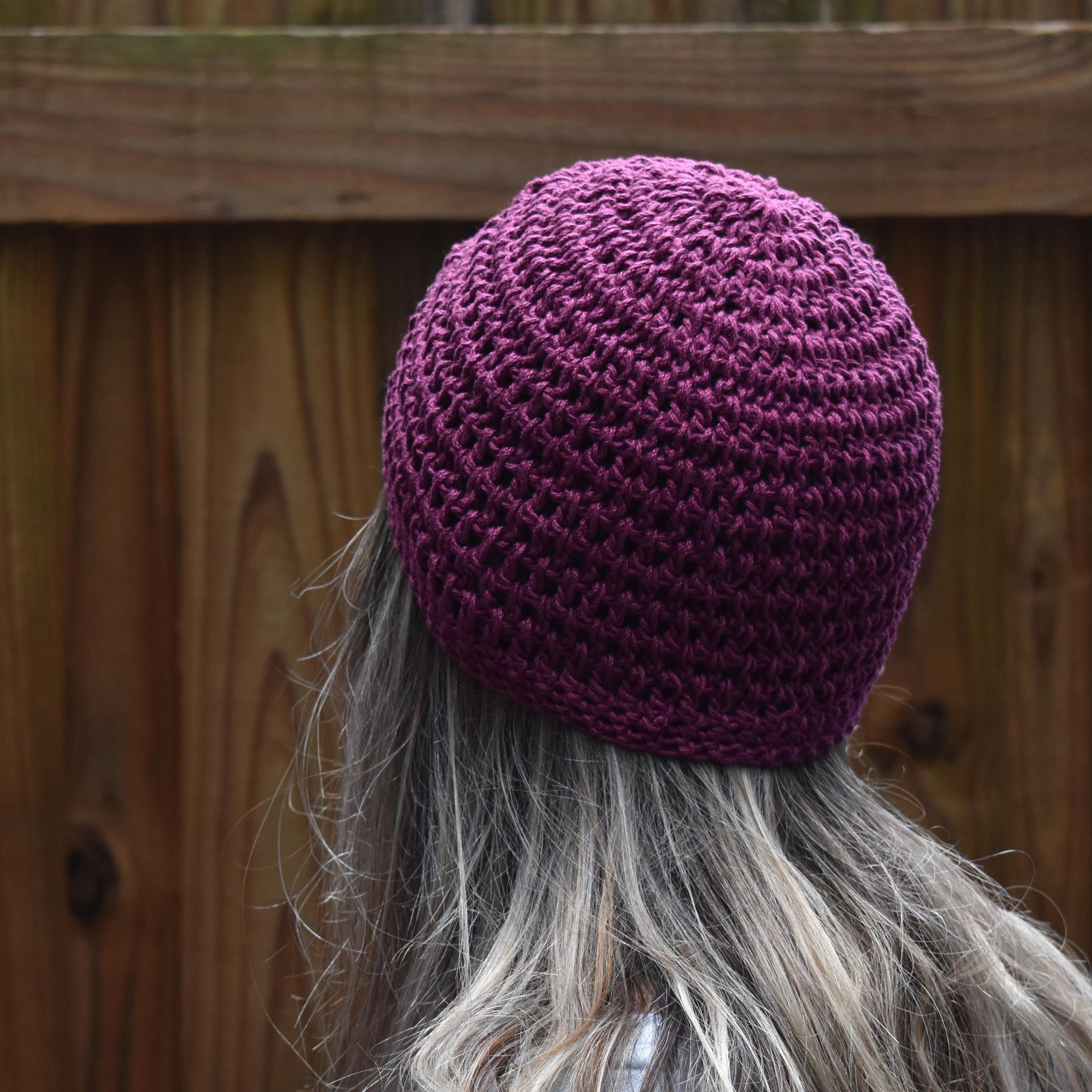 Purple knitted beanie worn by a person with gray hair, against a wooden fence background.