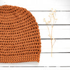 Orange knitted fabric on a white wooden surface with a small branch of dried flowers.