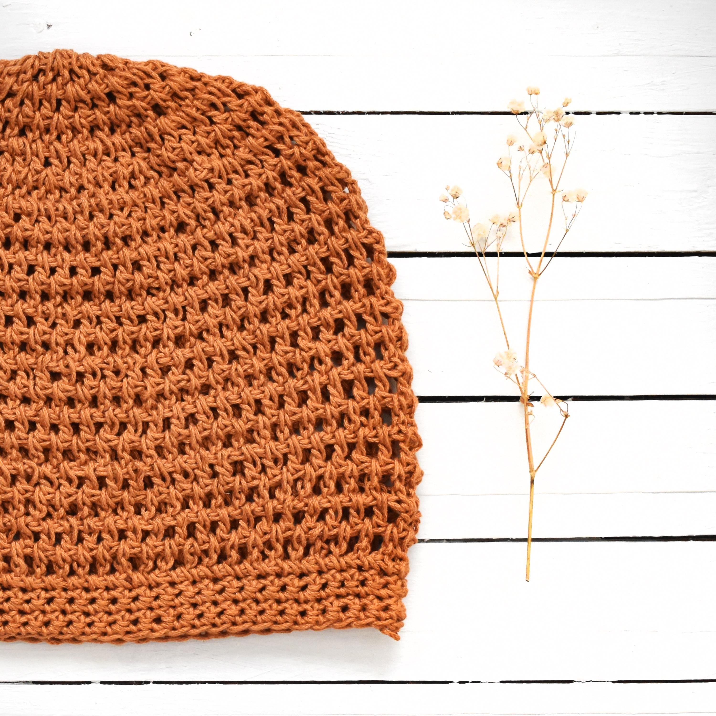 Orange knitted fabric on a white wooden surface with a small branch of dried flowers.