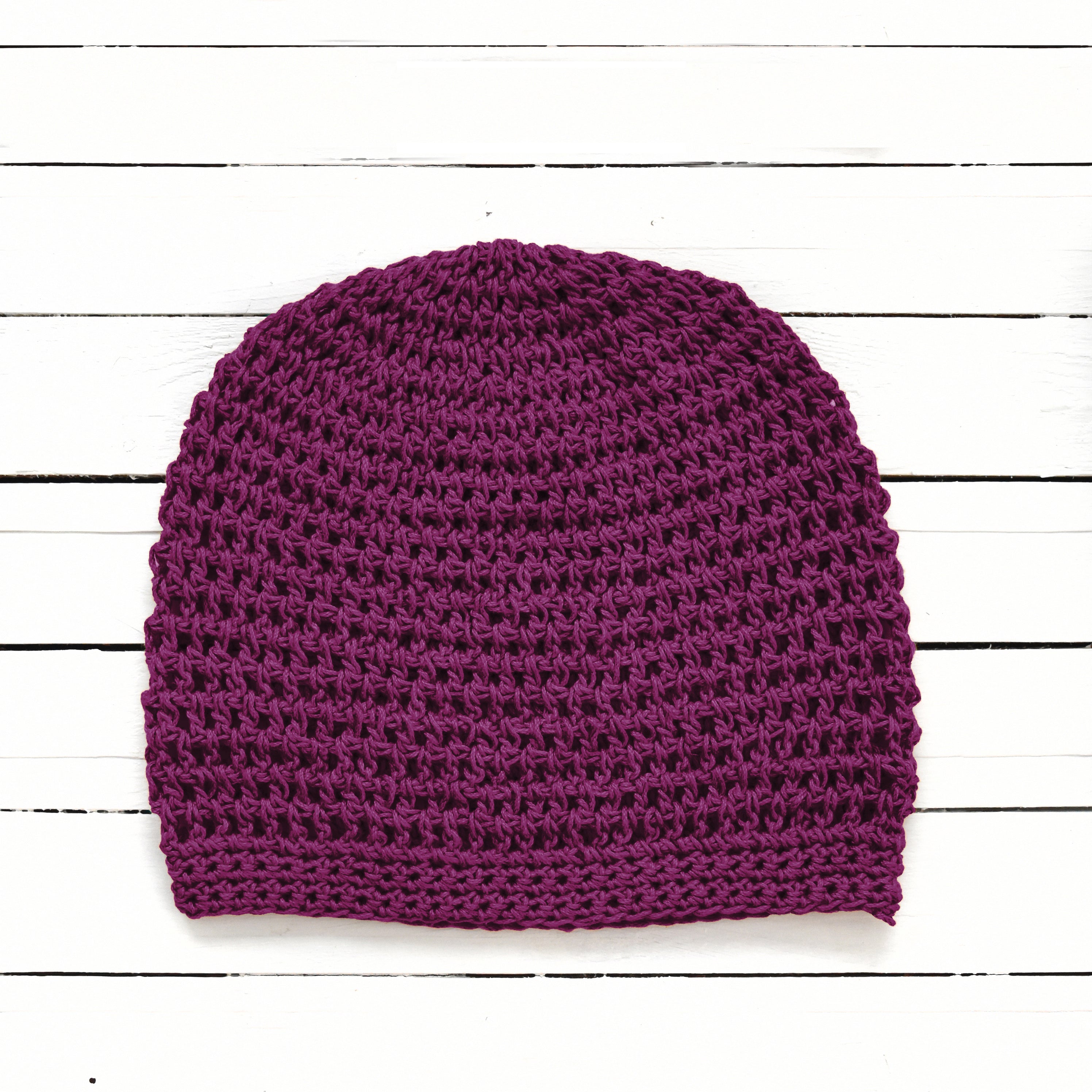 Dark purple knitted beanie on a white wooden surface.