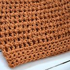 Close-up of an orange crocheted beanie on a white wooden surface.