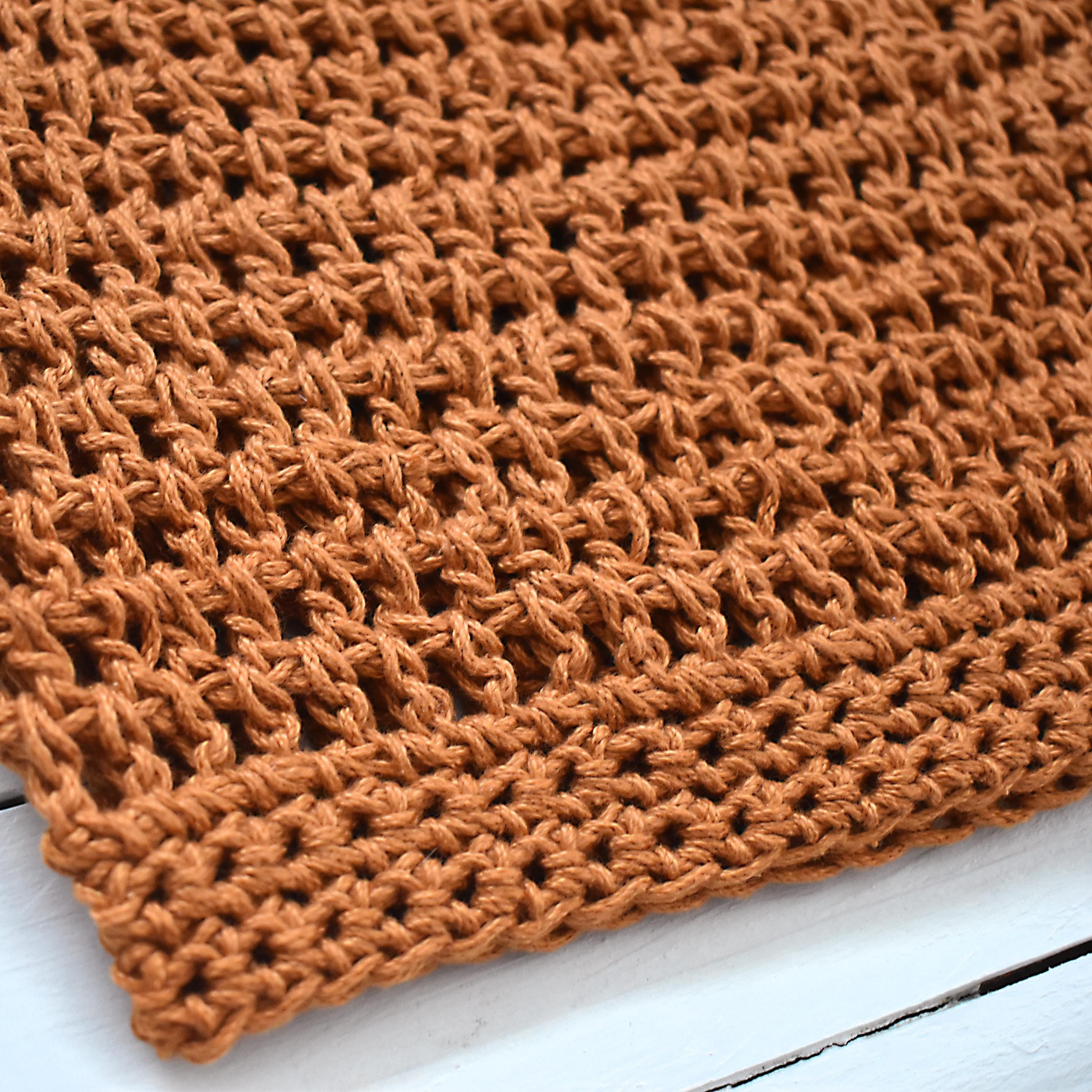 Close-up of an orange crocheted beanie on a white wooden surface.