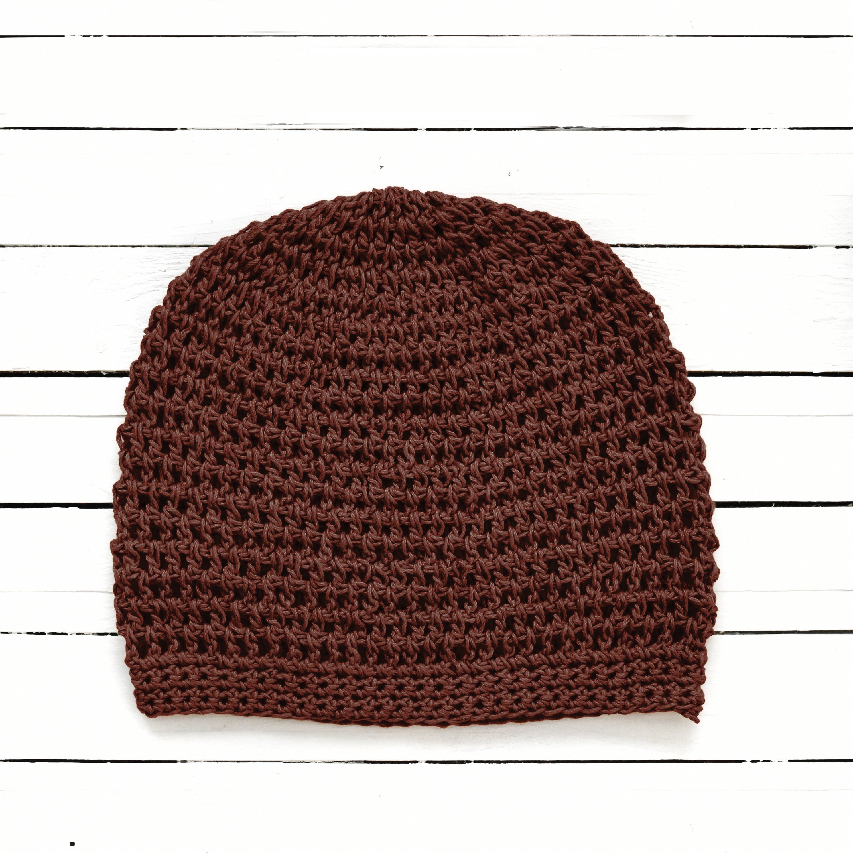 Brown knitted beanie on a white wooden surface.