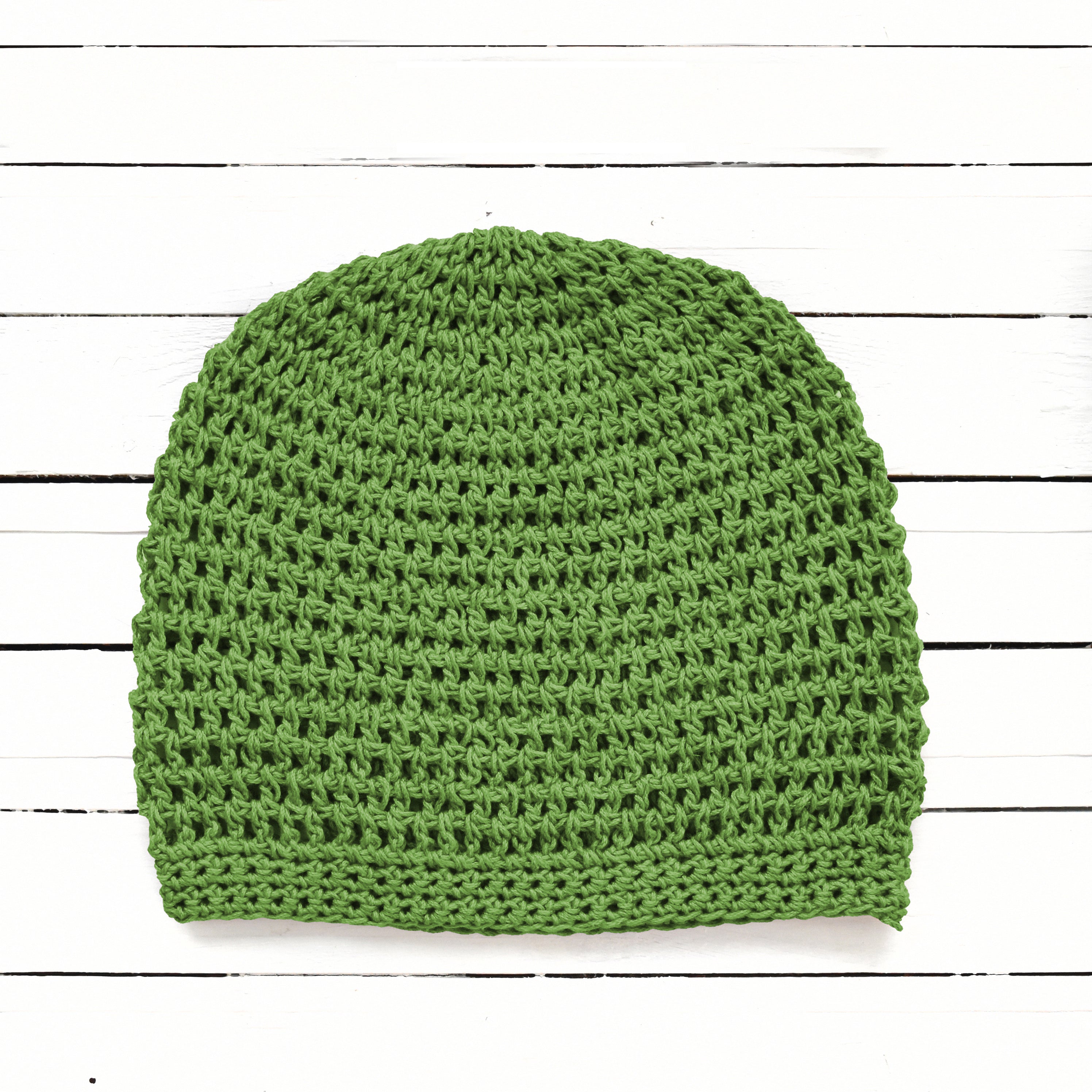 Green knitted beanie on a white wooden surface.