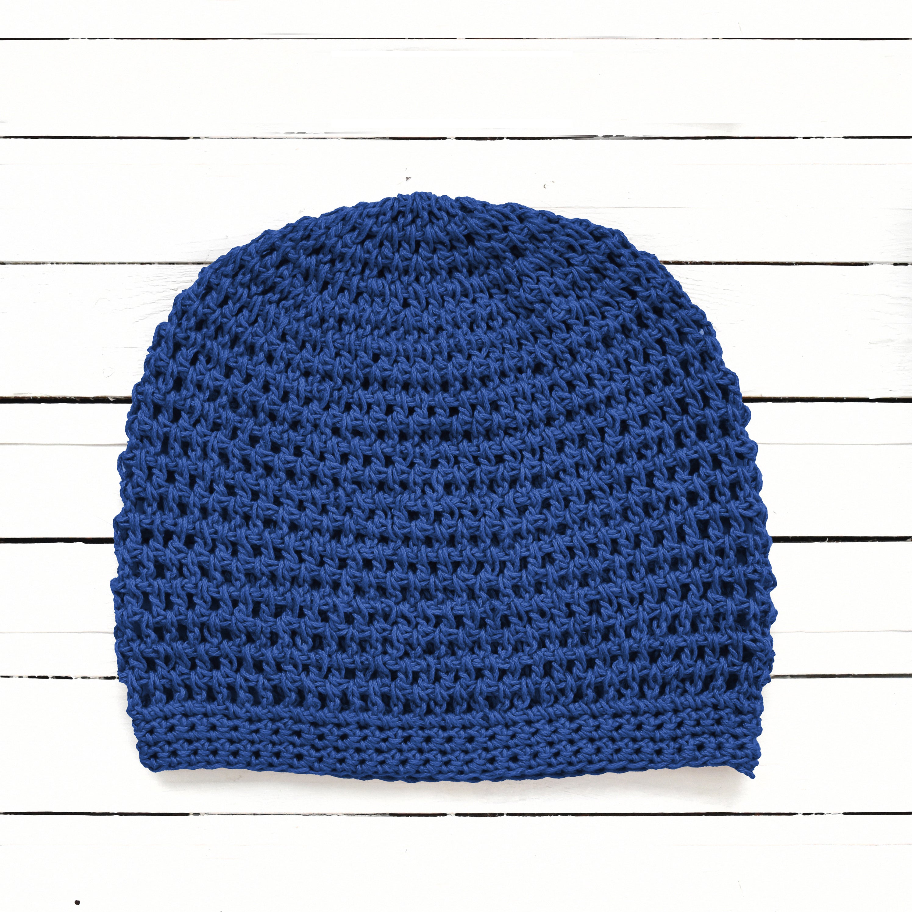 Blue crocheted beanie on a white wooden background.
