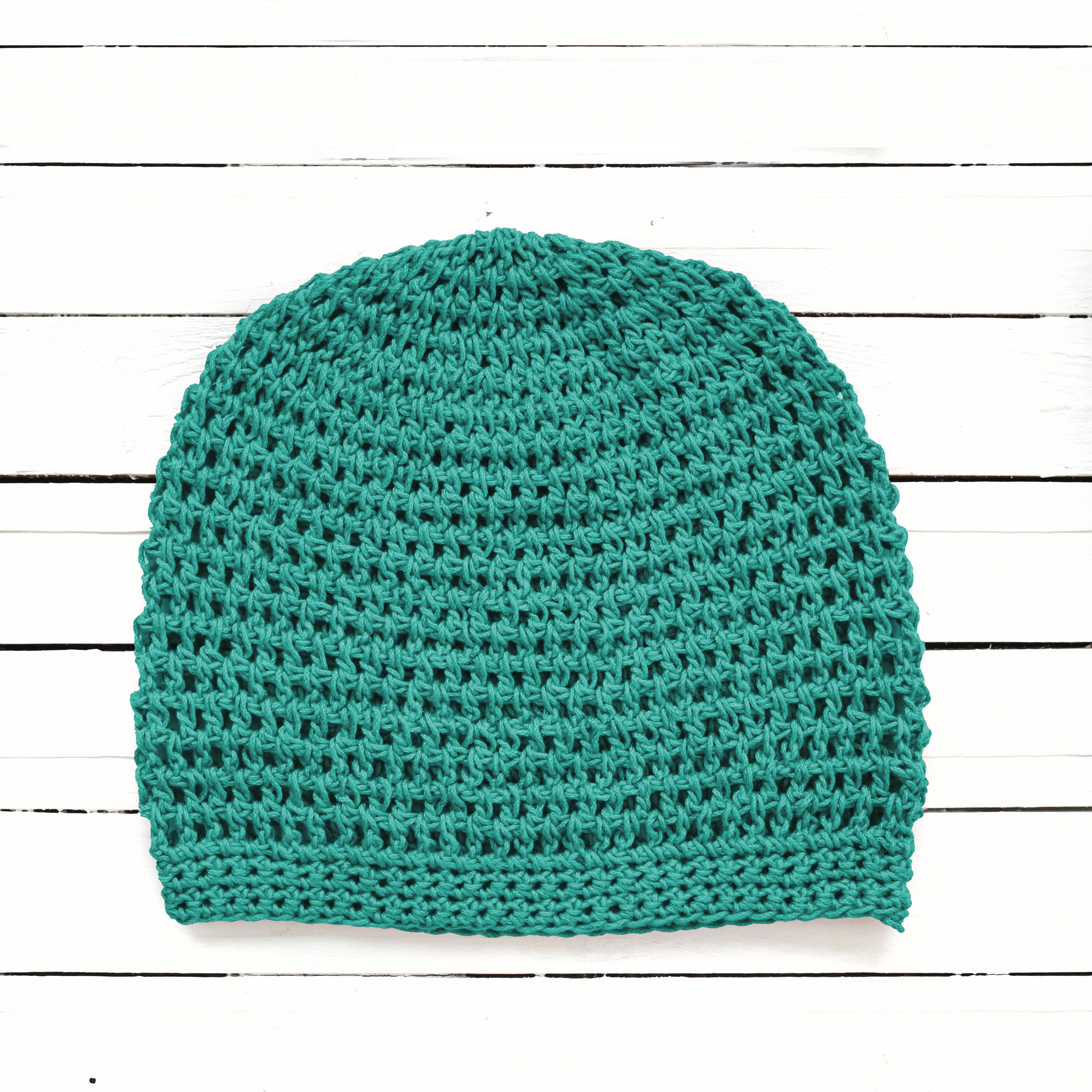 Teal crochet beanie on a white wooden background.