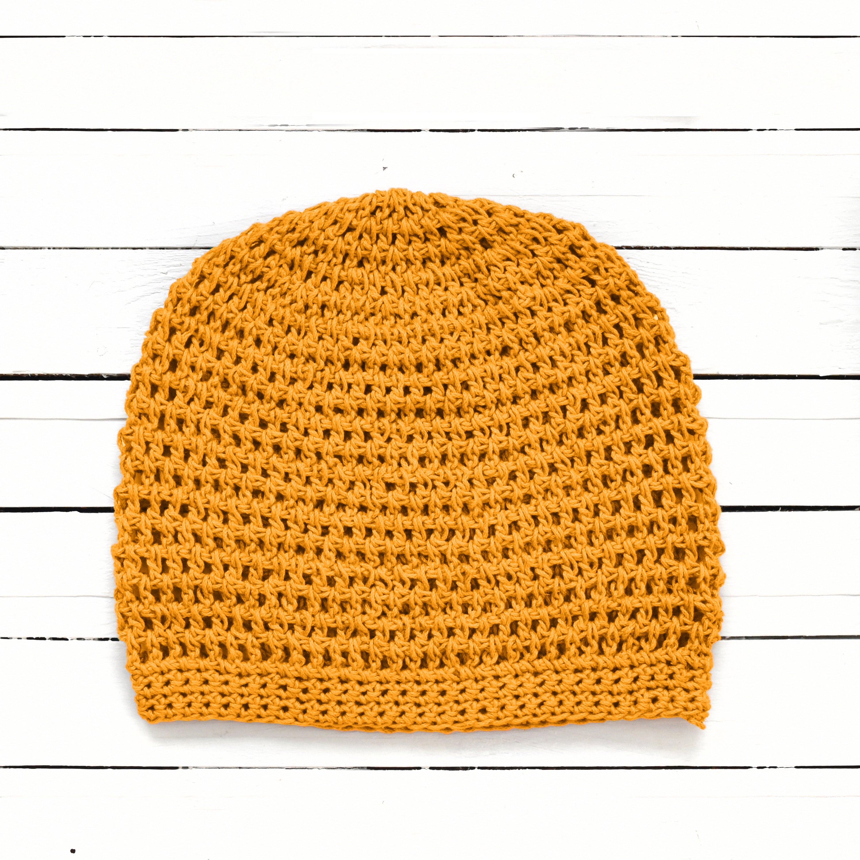 Yellow crochet beanie on a white wooden surface.