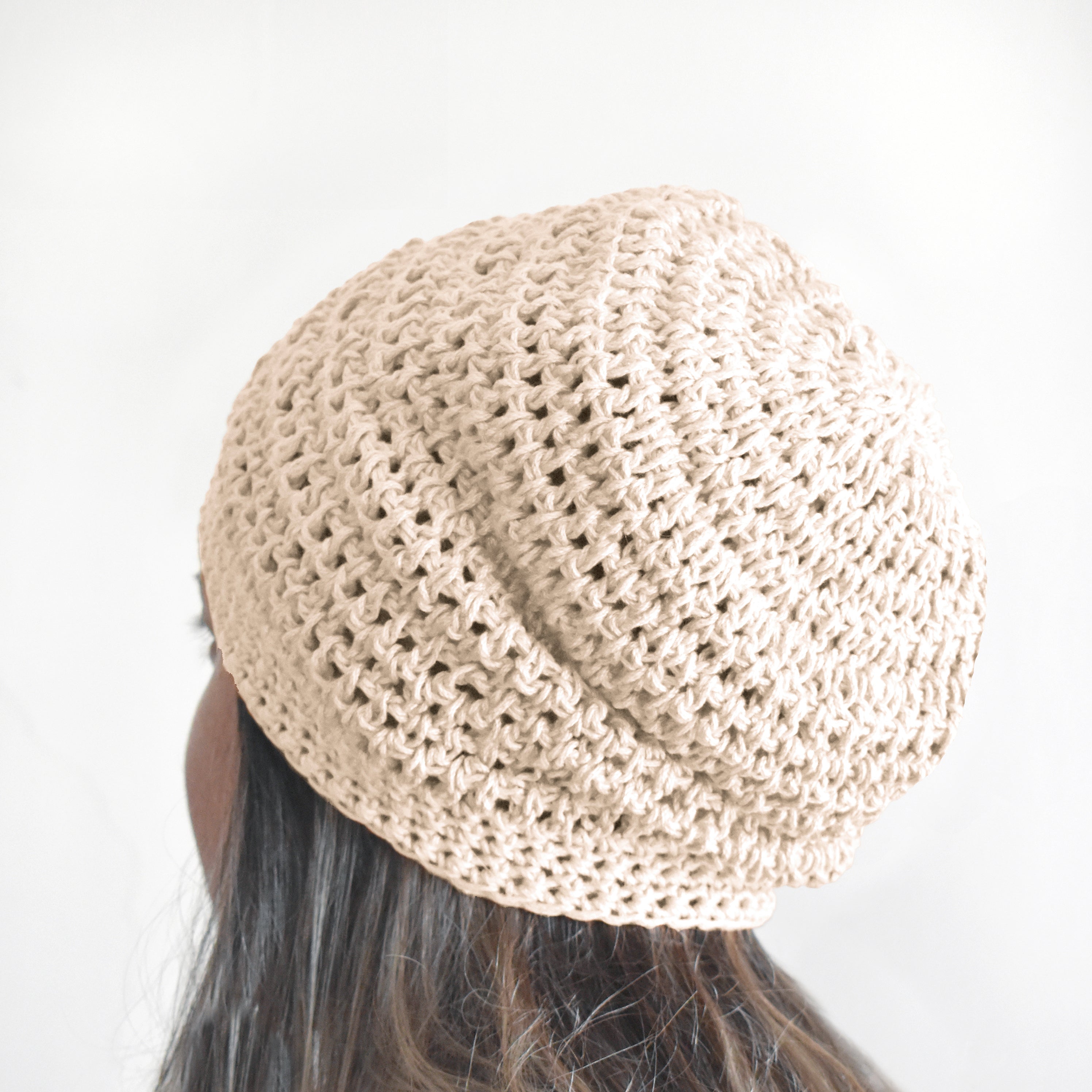 Beige crochet hat worn by a person with dark hair on a white background.