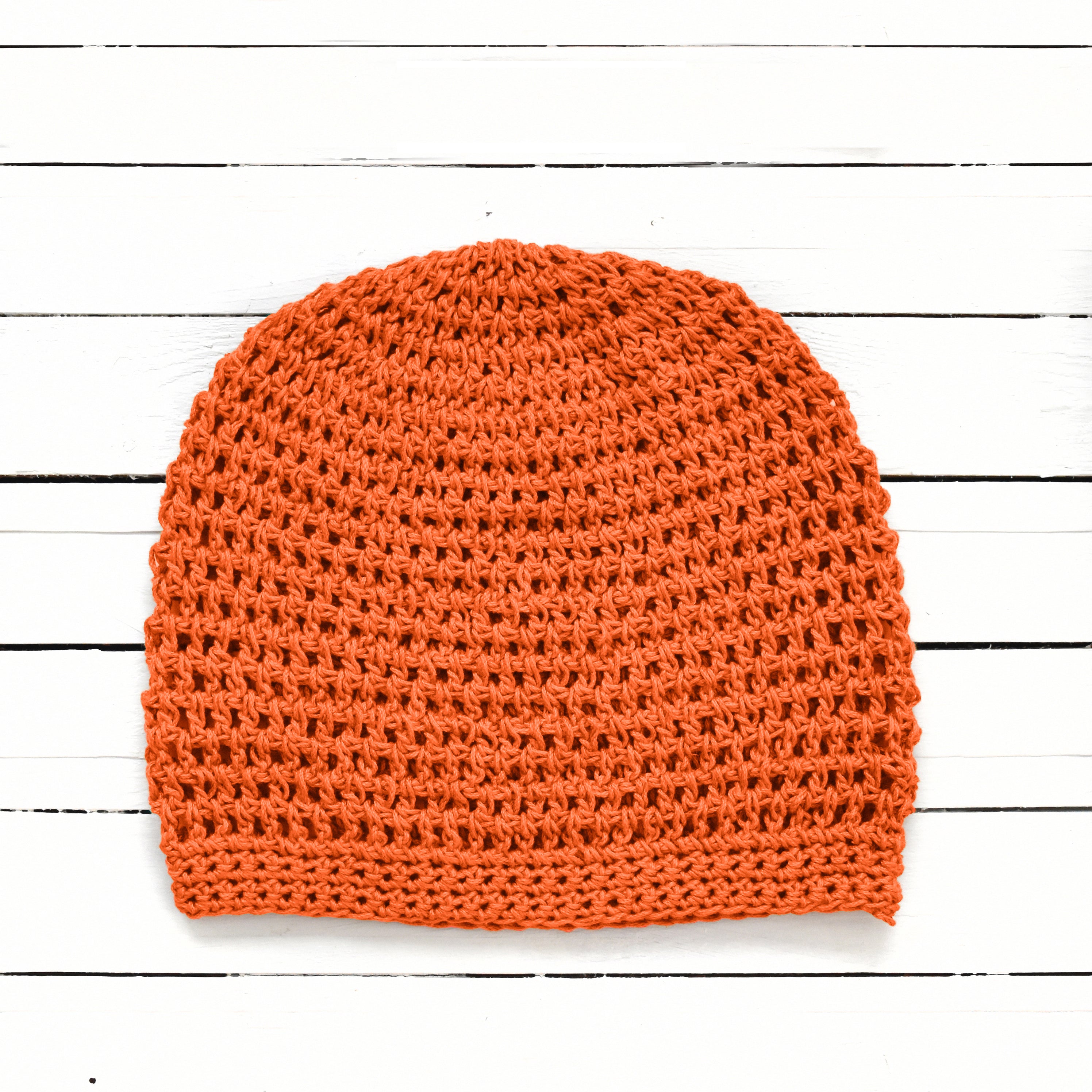Orange crochet beanie on a white wooden surface.