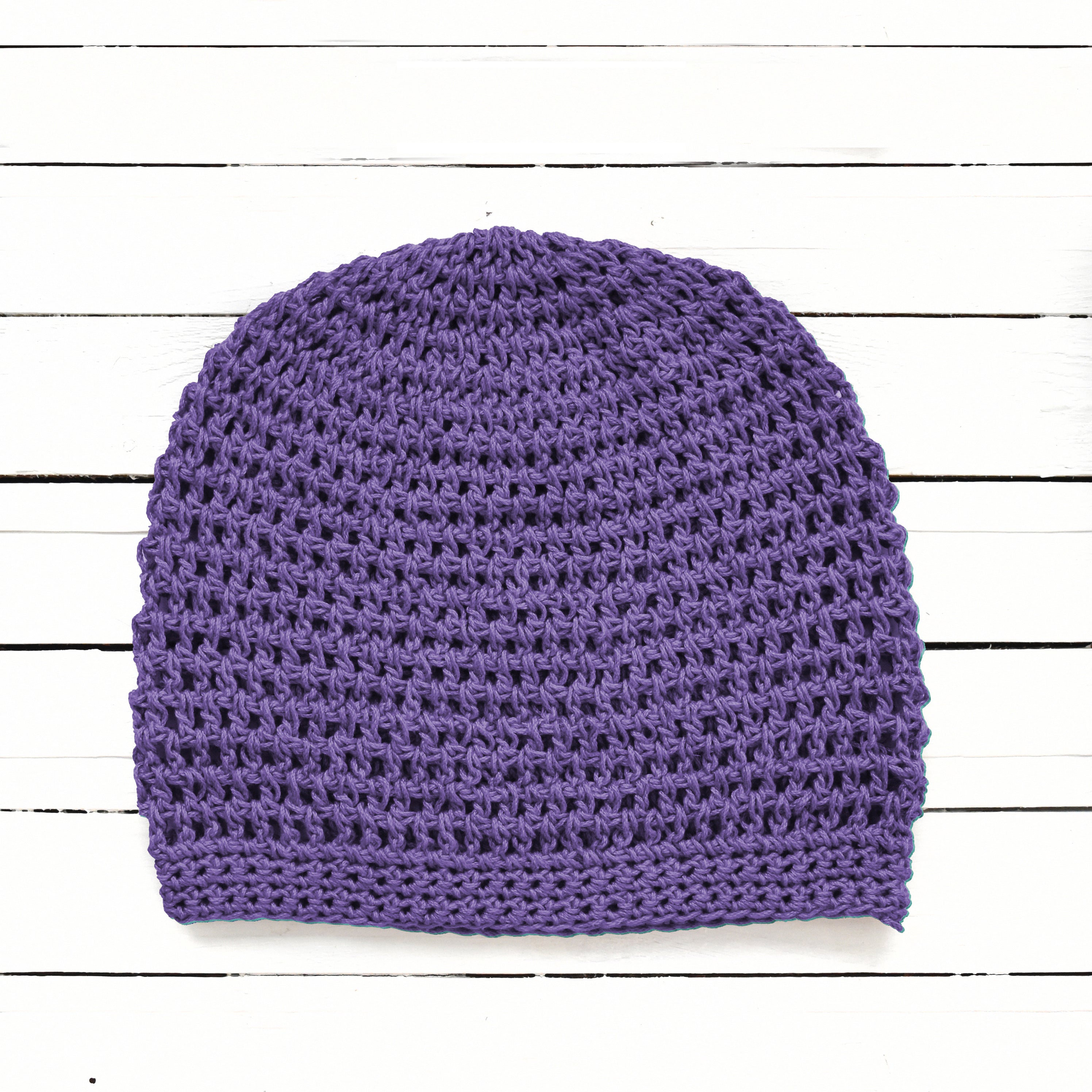 Purple crocheted beanie on a white wooden background.