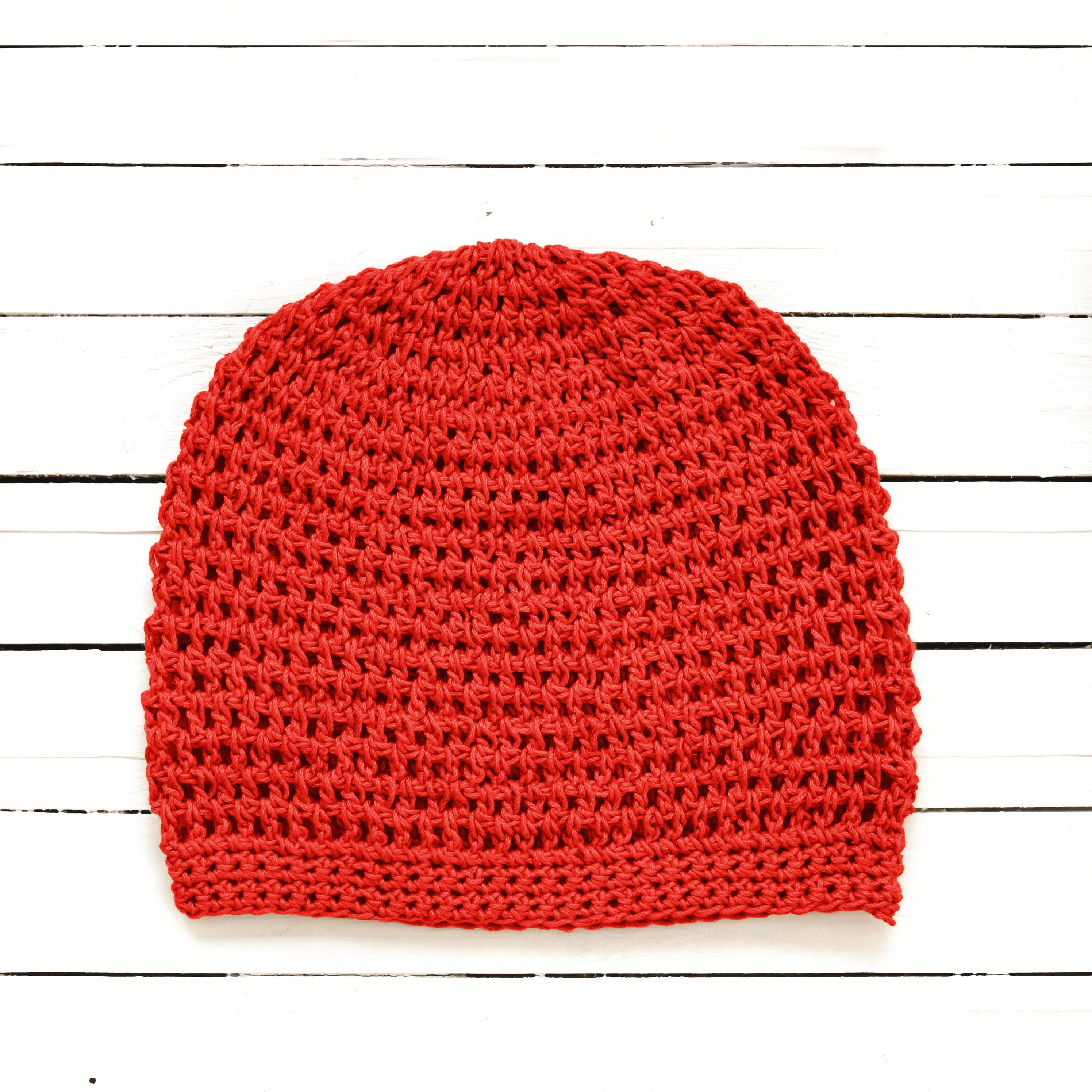 Red knitted beanie on a white wooden surface.