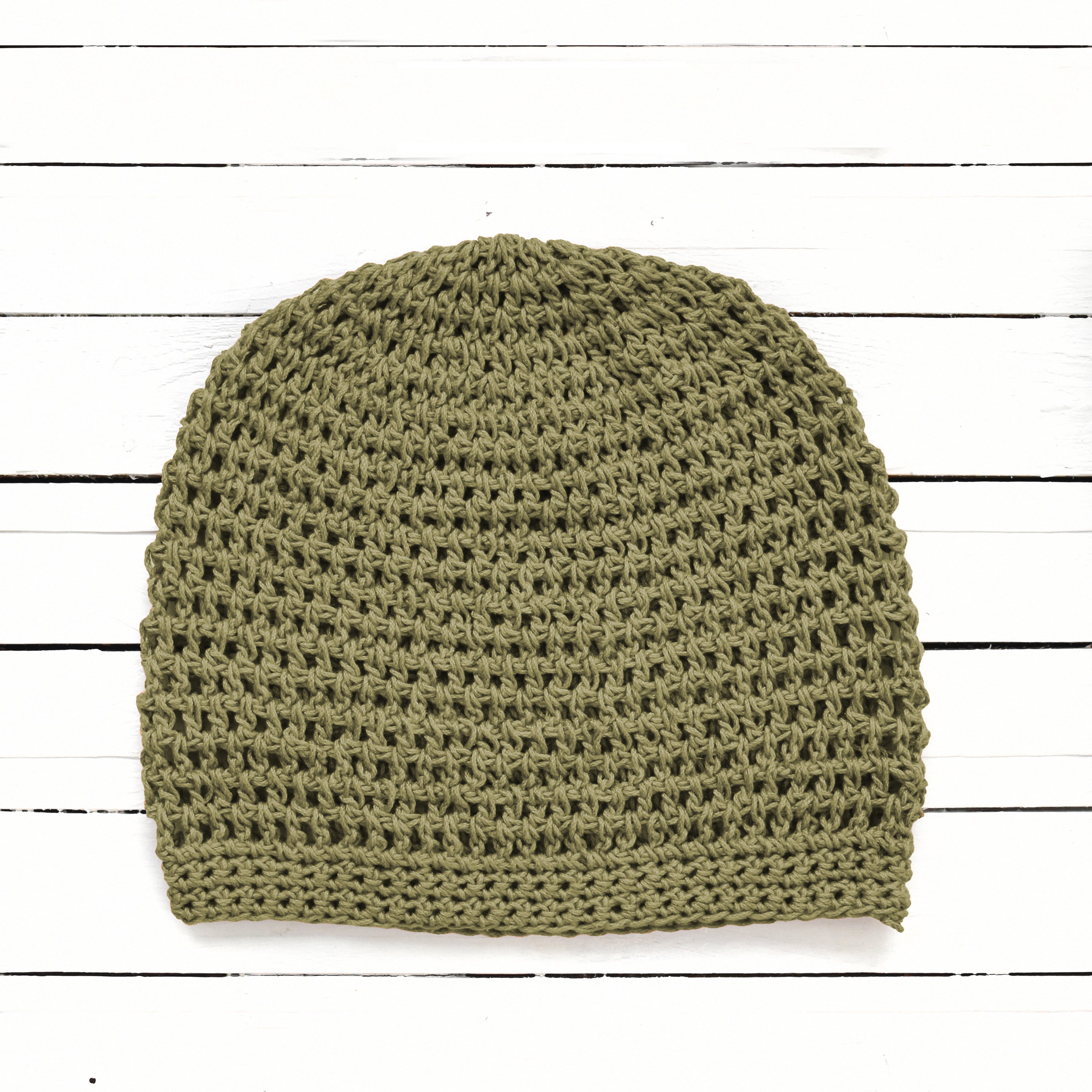 Green crochet beanie on a white wooden surface.