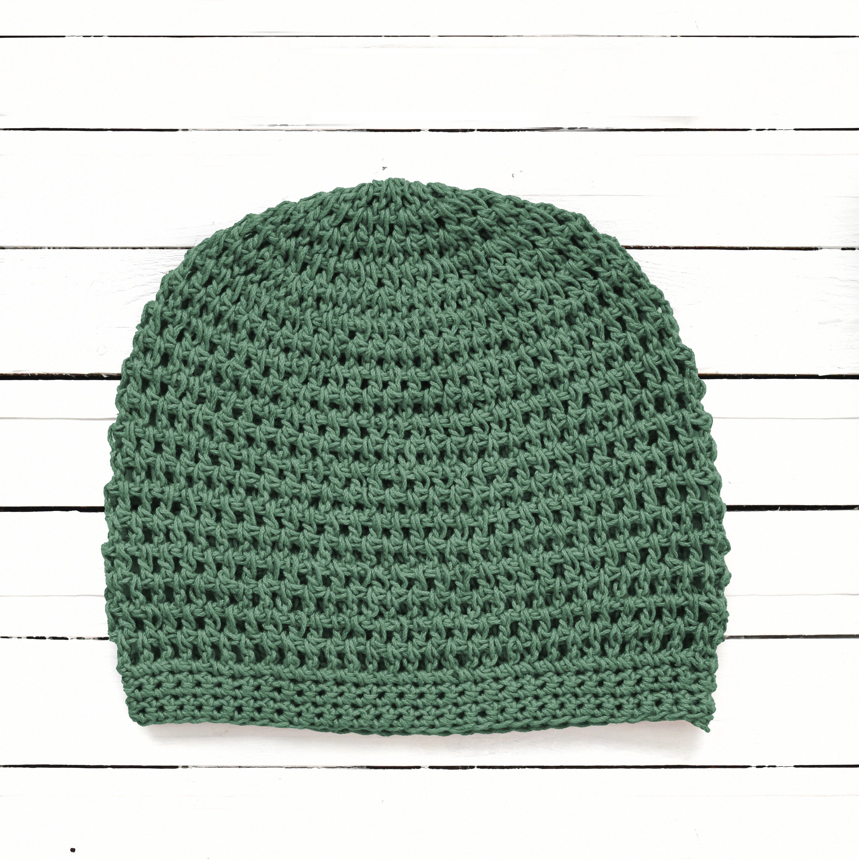 Earthy green handmade crochet beanie on a white wooden background.