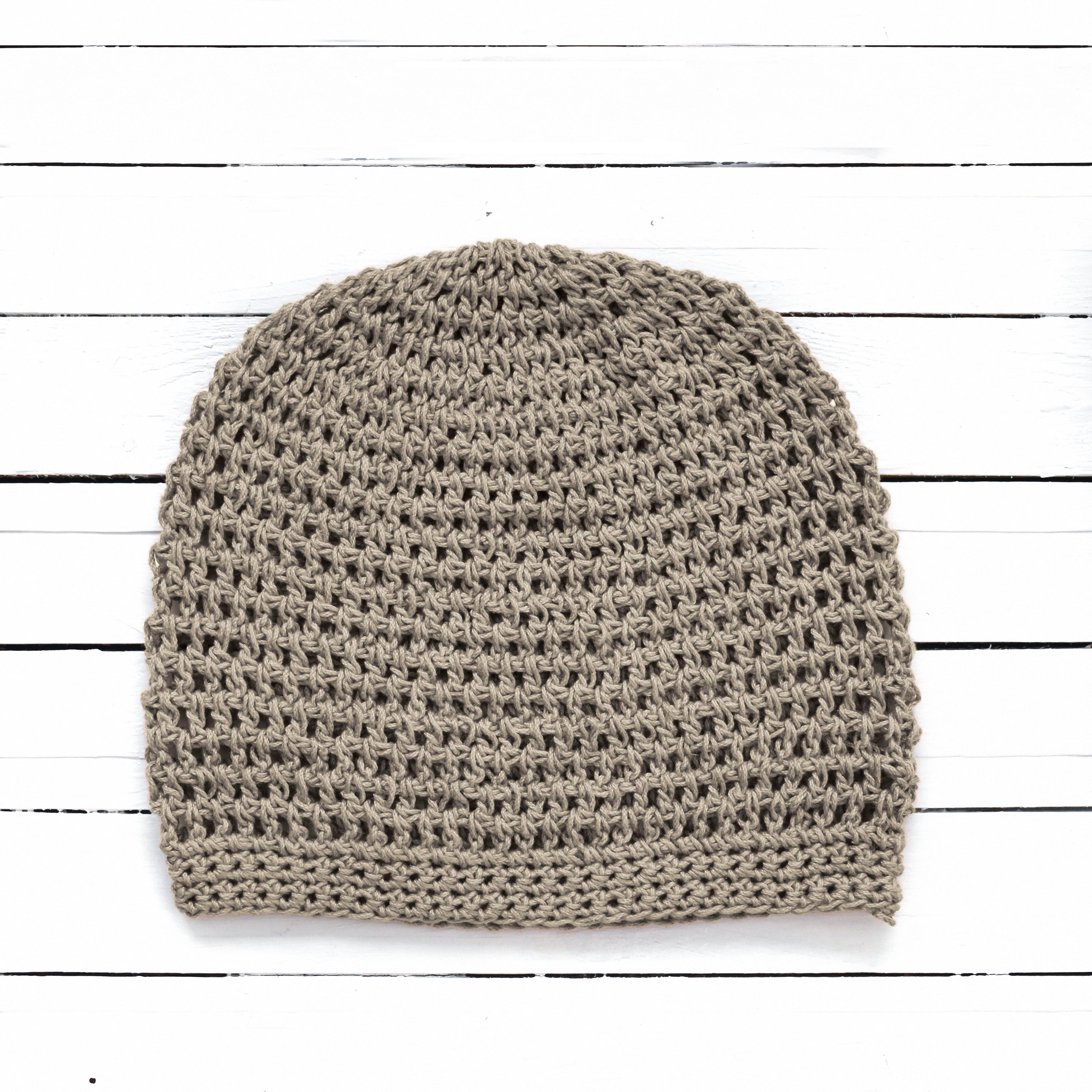 Light brown crochet beanie on a white wooden surface.