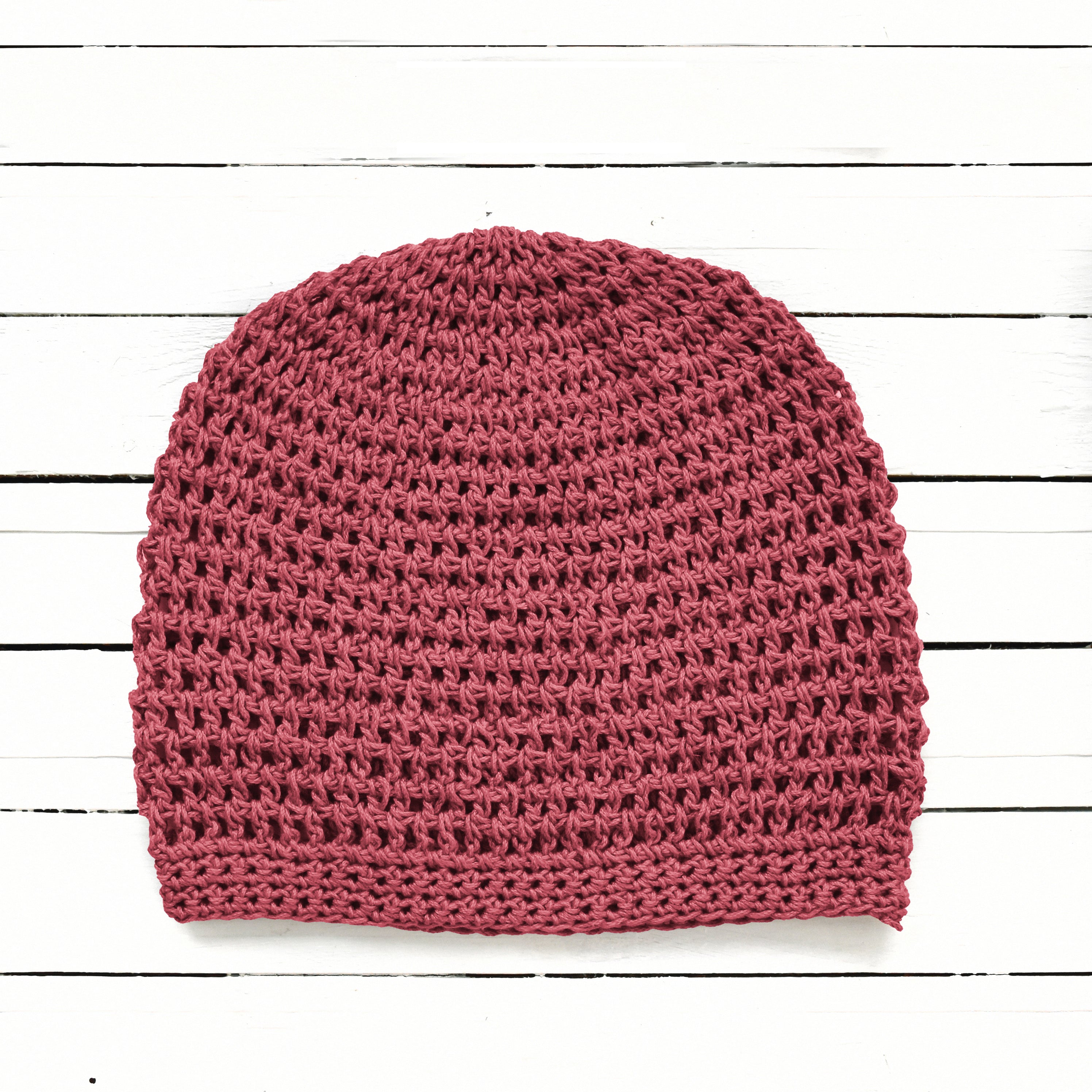 Terracotta pink handmade slouchy beanie on a white wooden background.