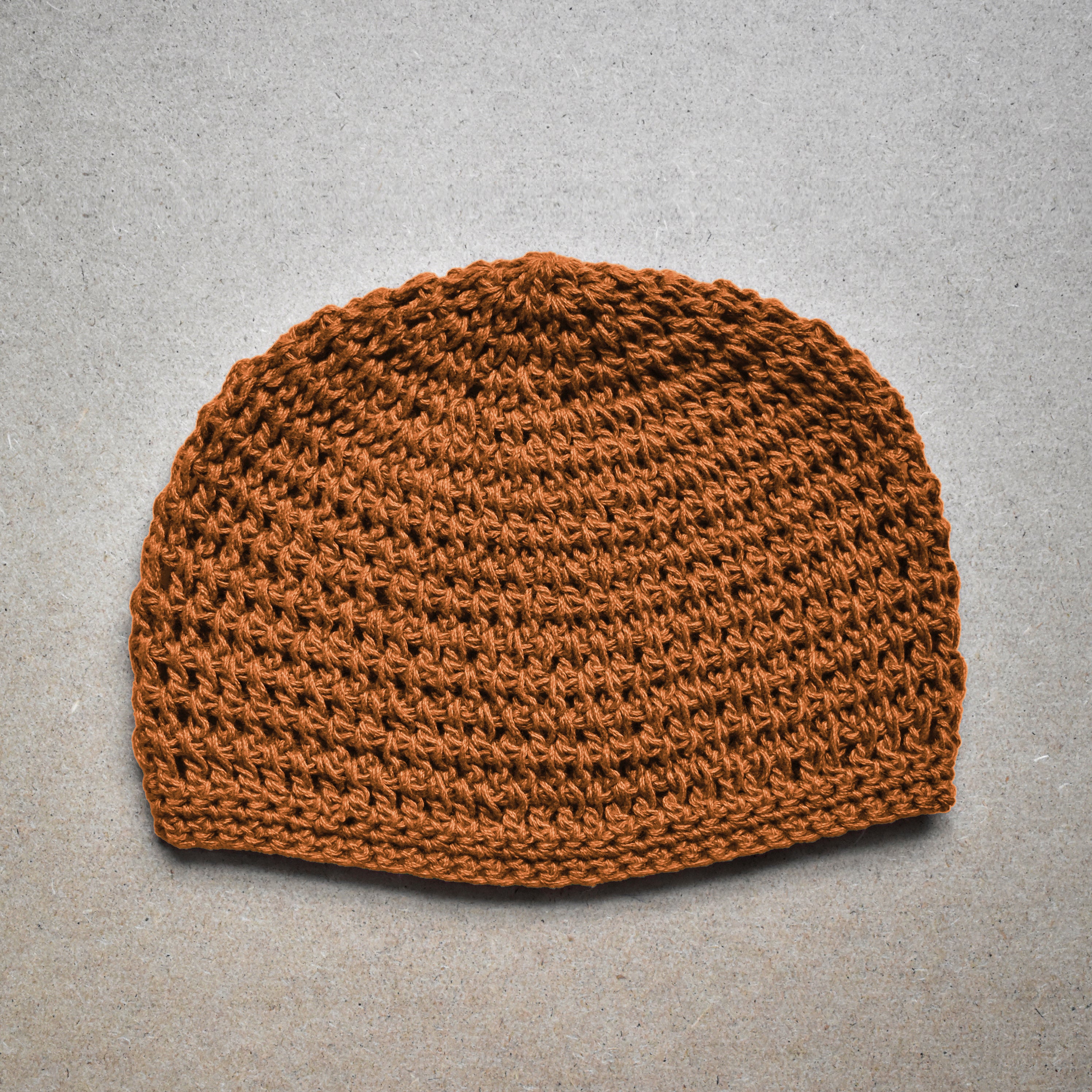 Amber brown knitted beanie on a neutral kraft background.