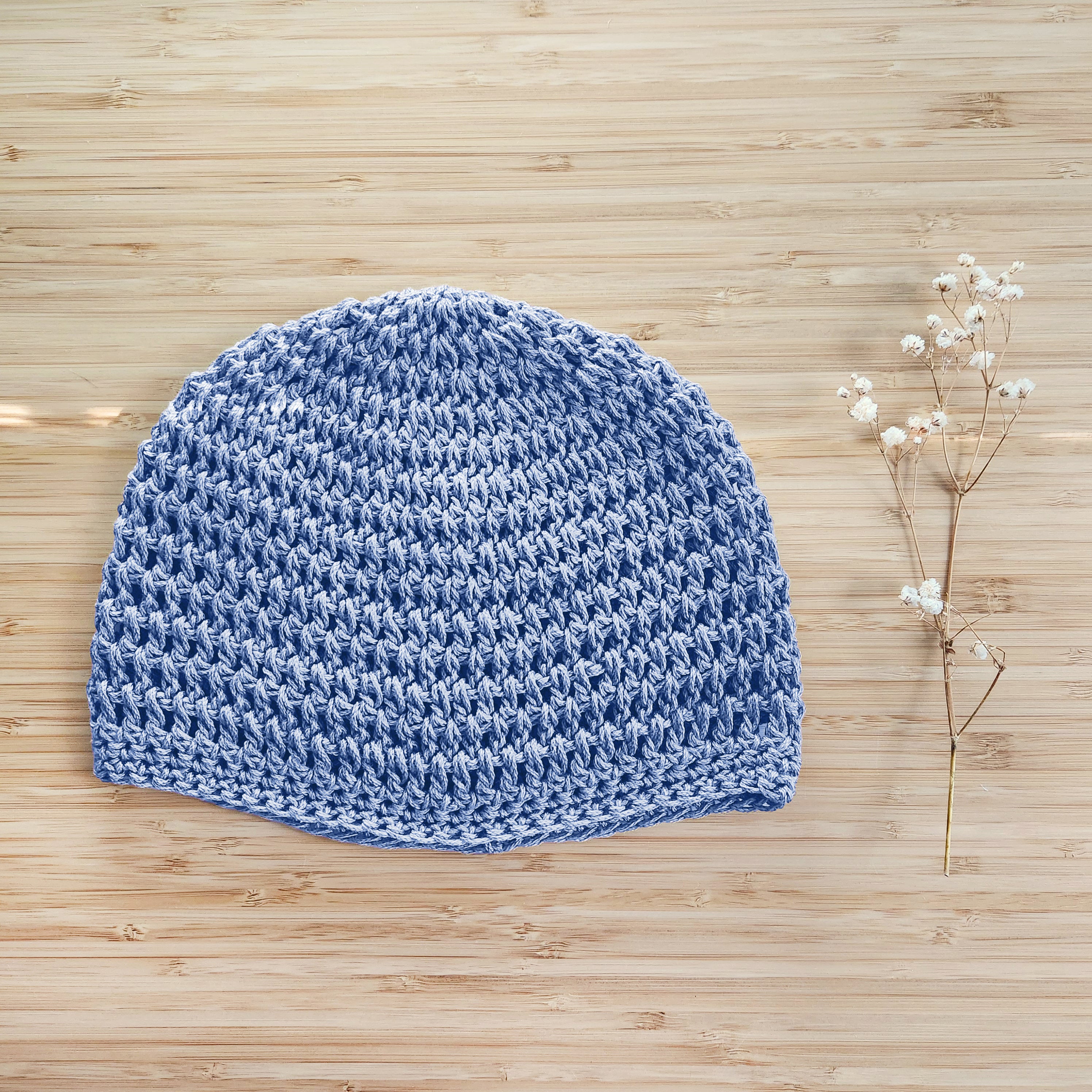 Baby blue knitted beanie on a wooden surface with a small branch of flowers.