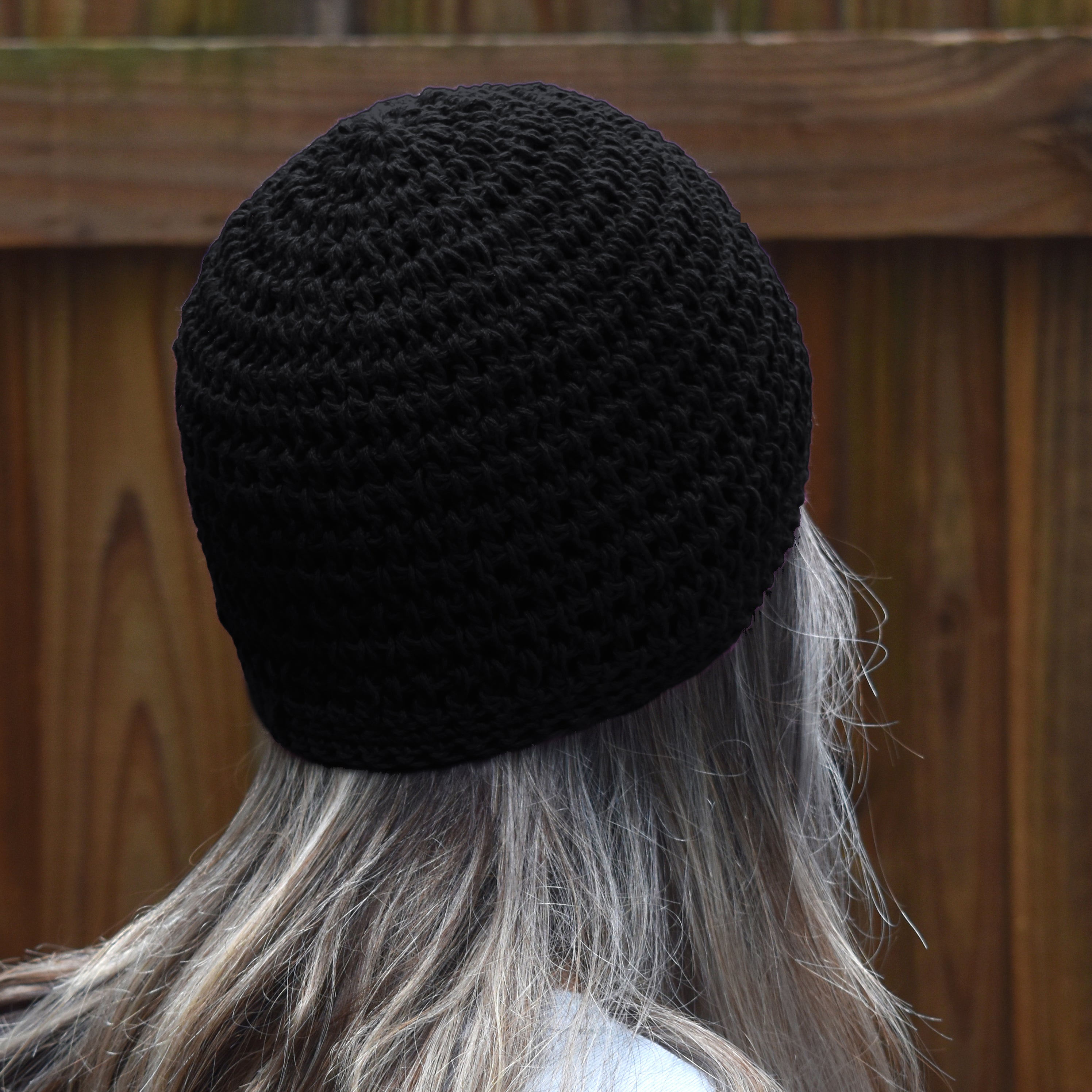 Person wearing a black knitted beanie with a wooden fence background.