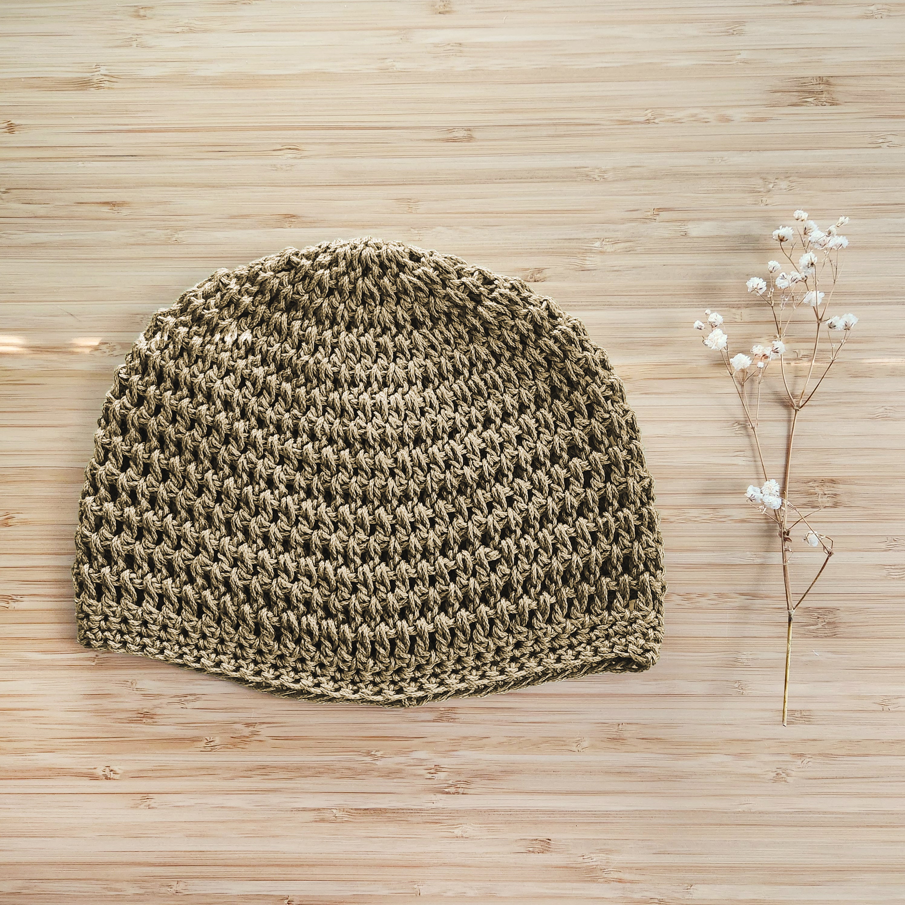 Light brown knitted beanie on a wooden surface with a small branch of flowers.