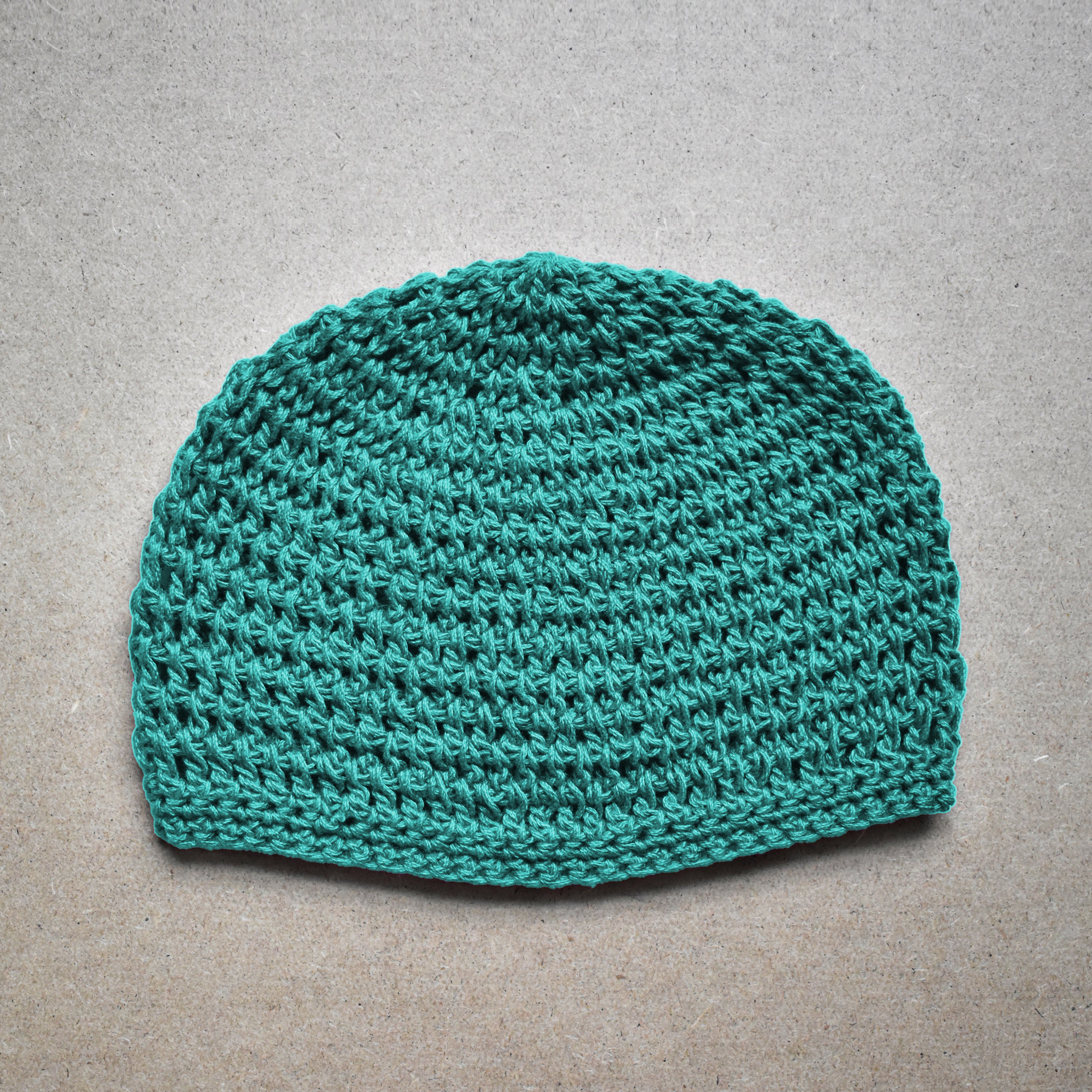 Teal knitted beanie on a gray background.