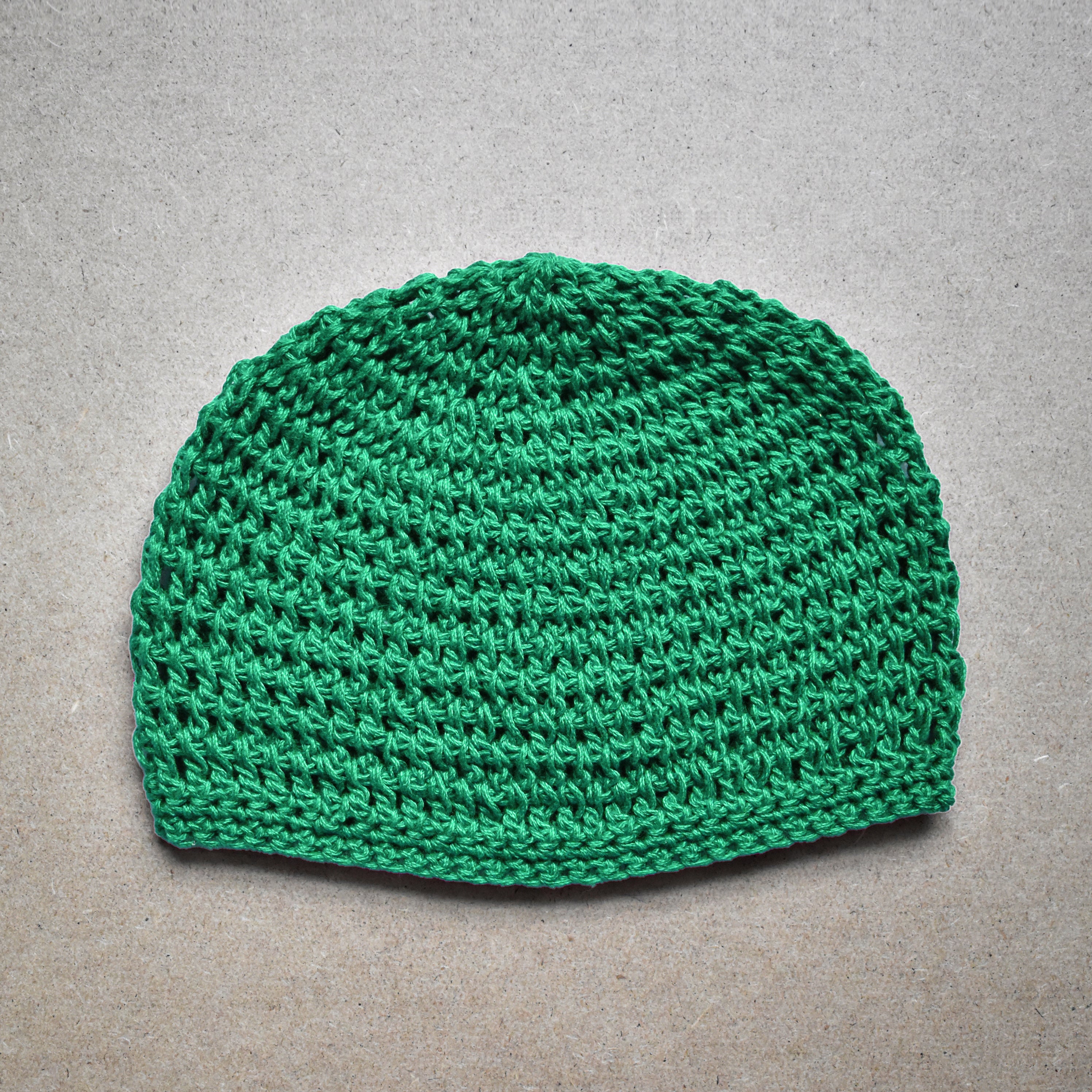 Green knitted beanie on a gray background.