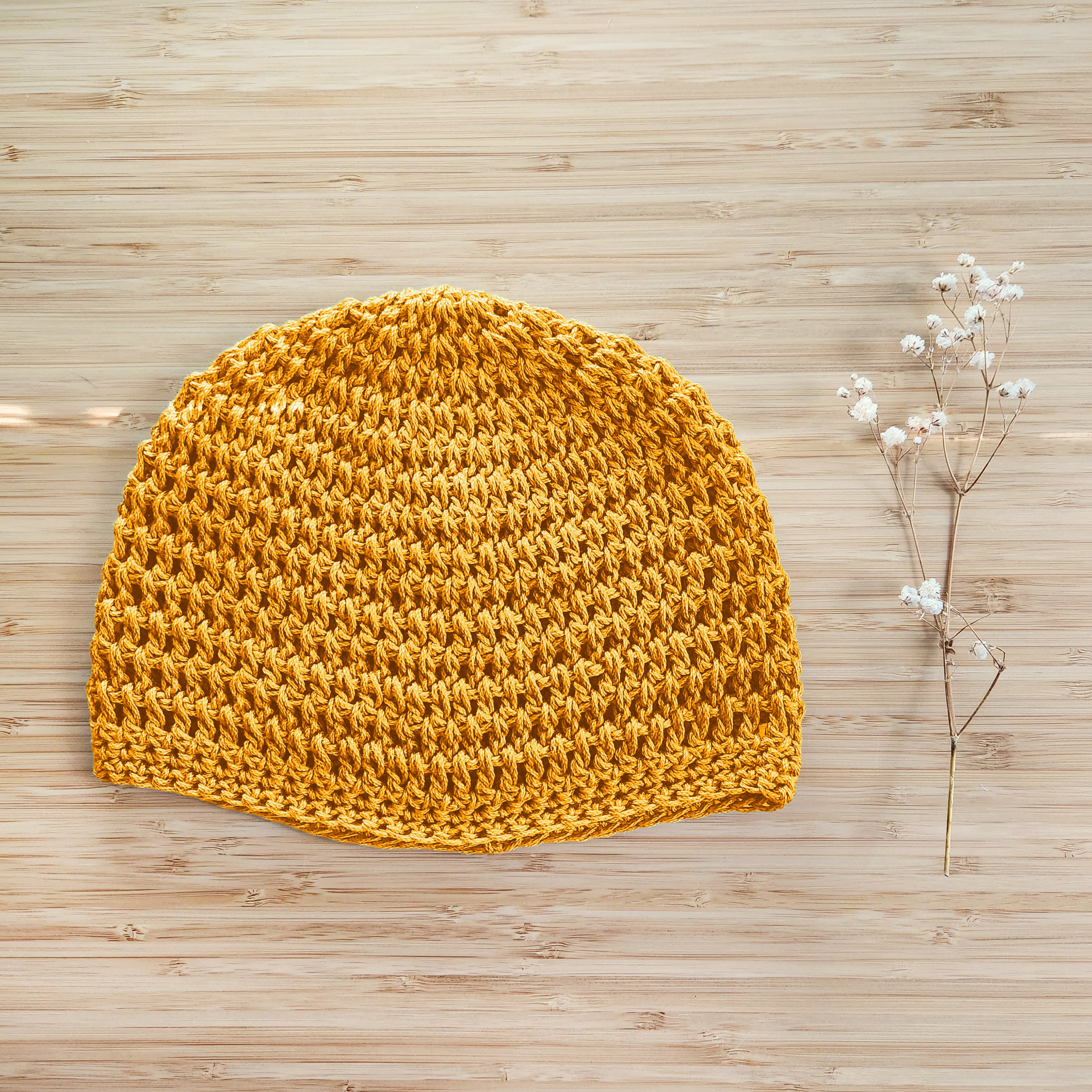 Yellow knitted beanie on a wooden surface with a small branch of flowers.