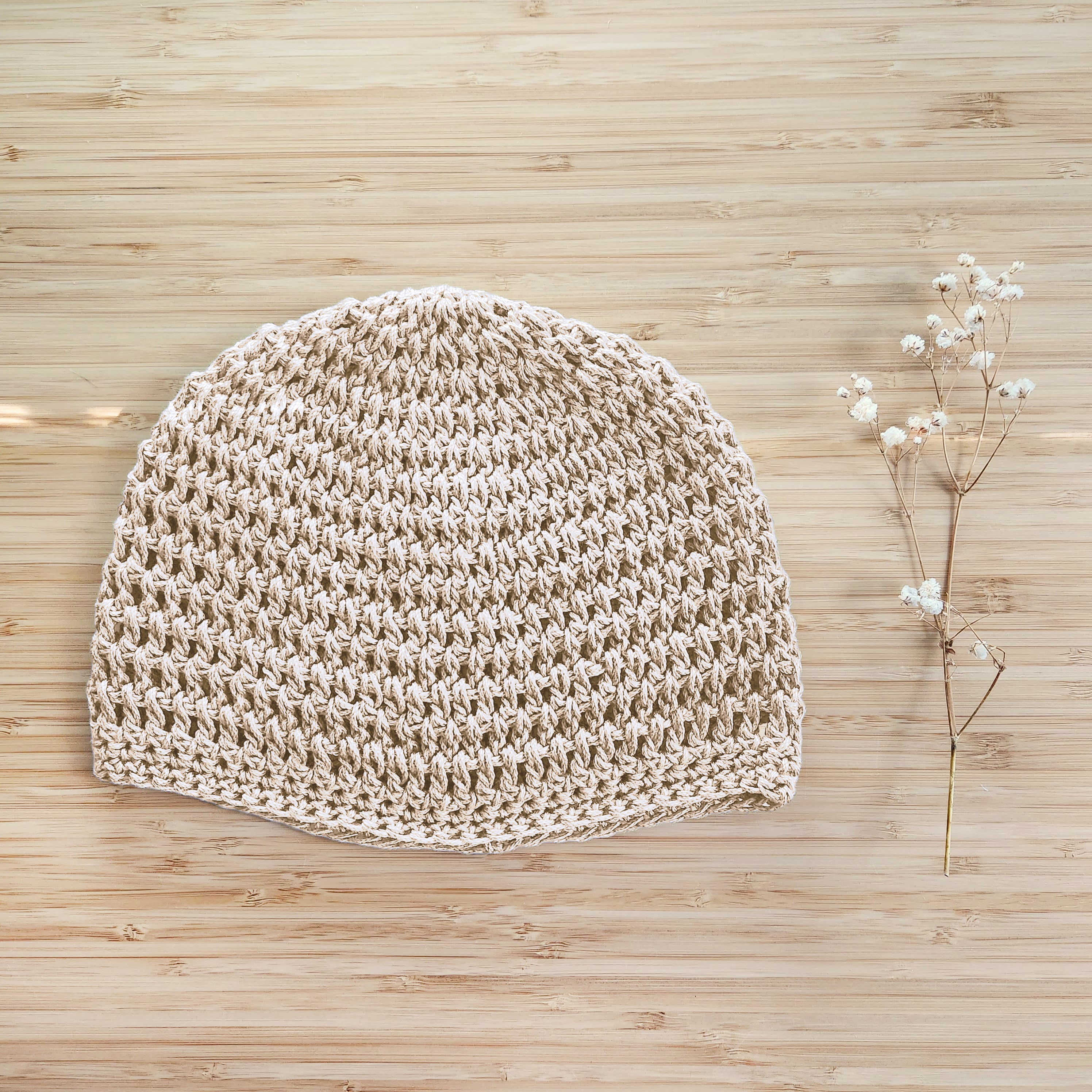 Beige crochet hat on a wooden surface with a small branch of flowers.