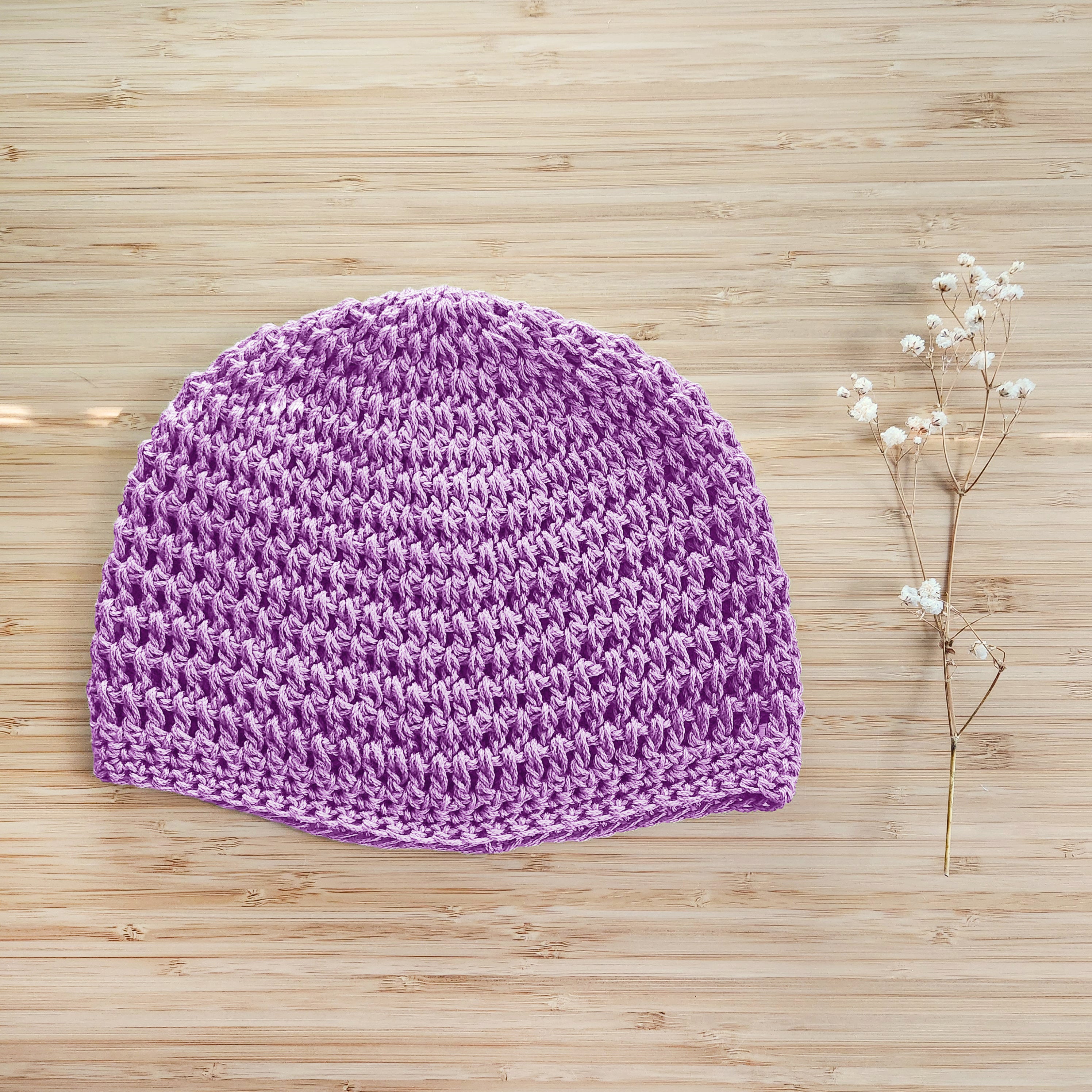 Light purple knitted hat on a wooden surface with a small branch of flowers.