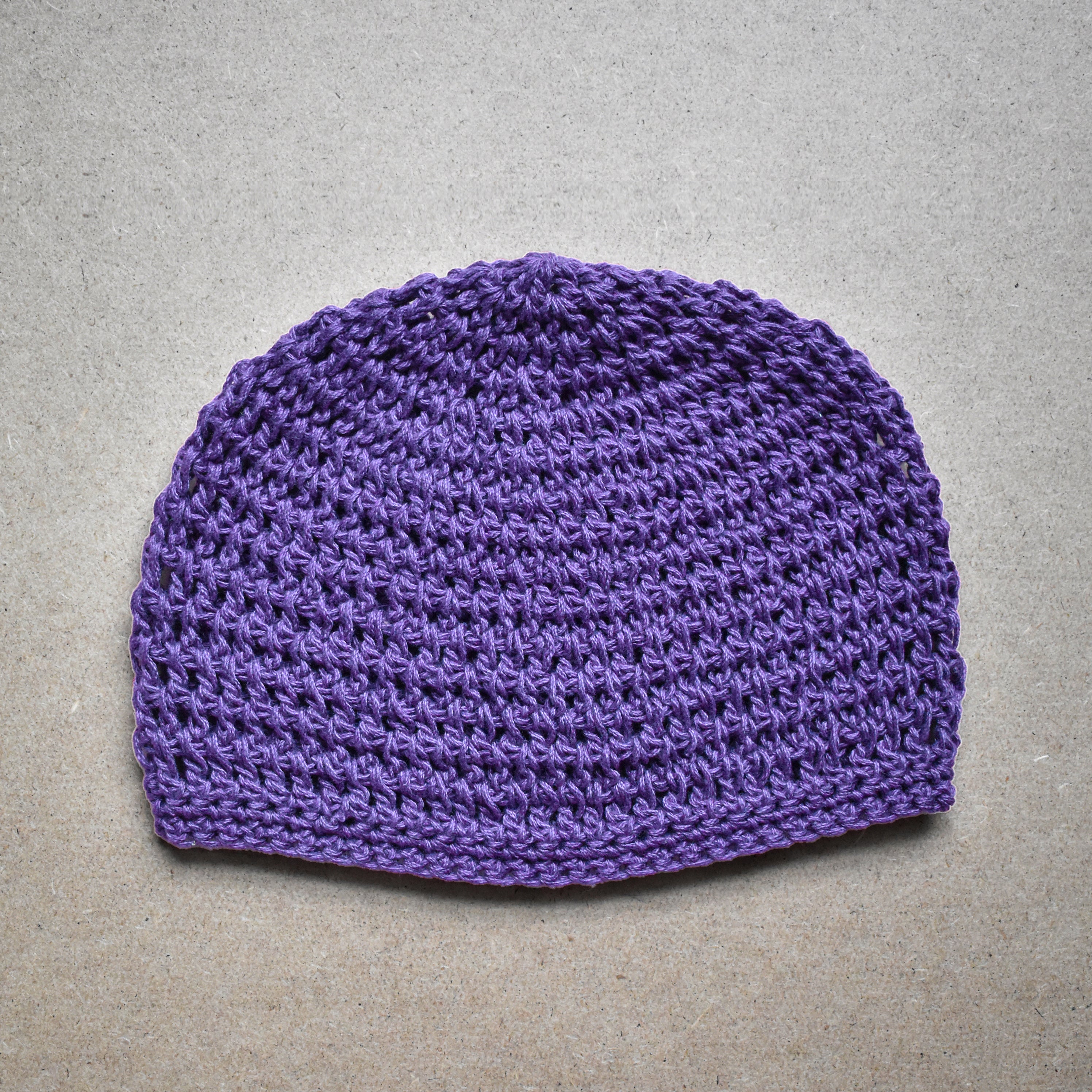 Purple knitted beanie on a textured gray background.