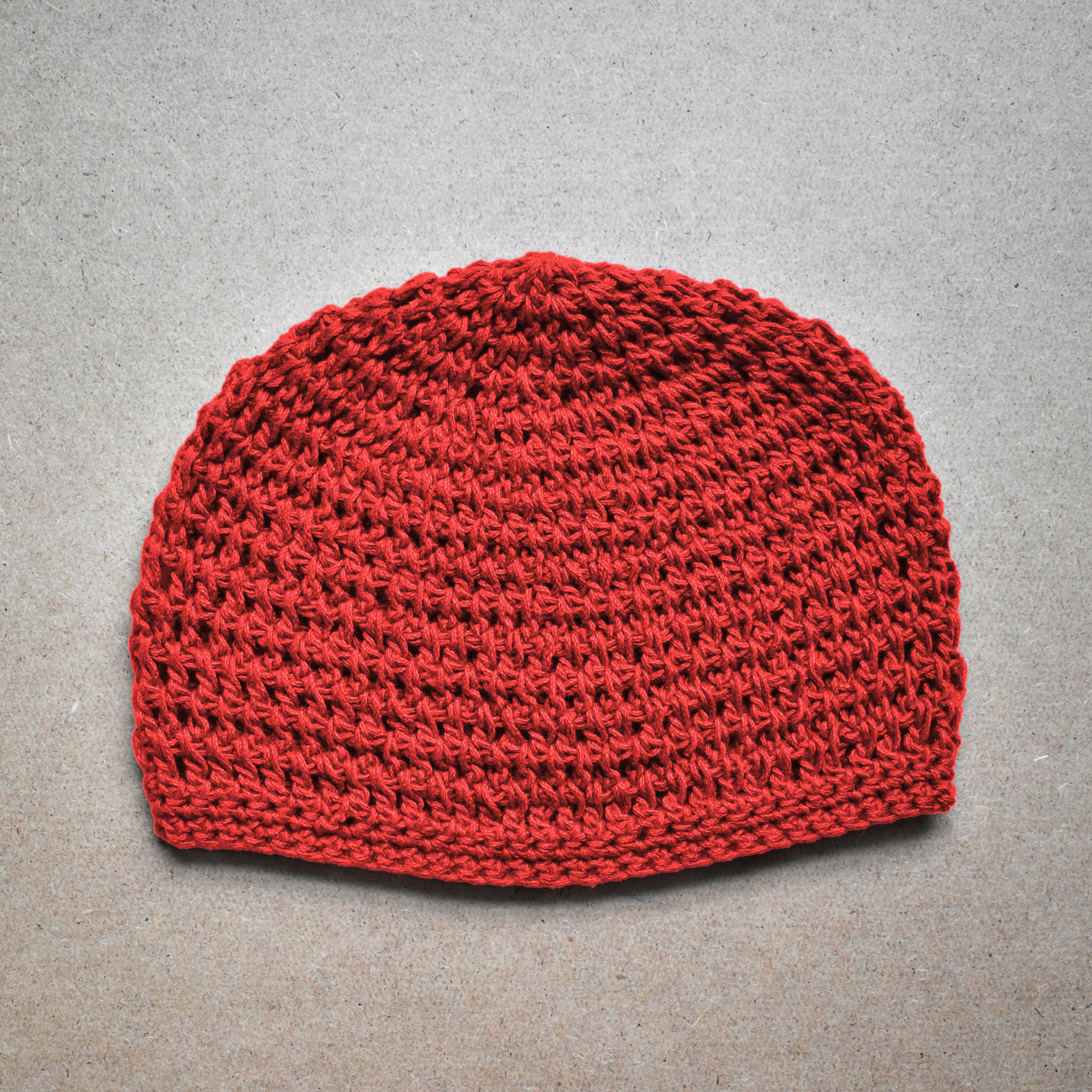 Red knitted beanie on a neutral kraft background.