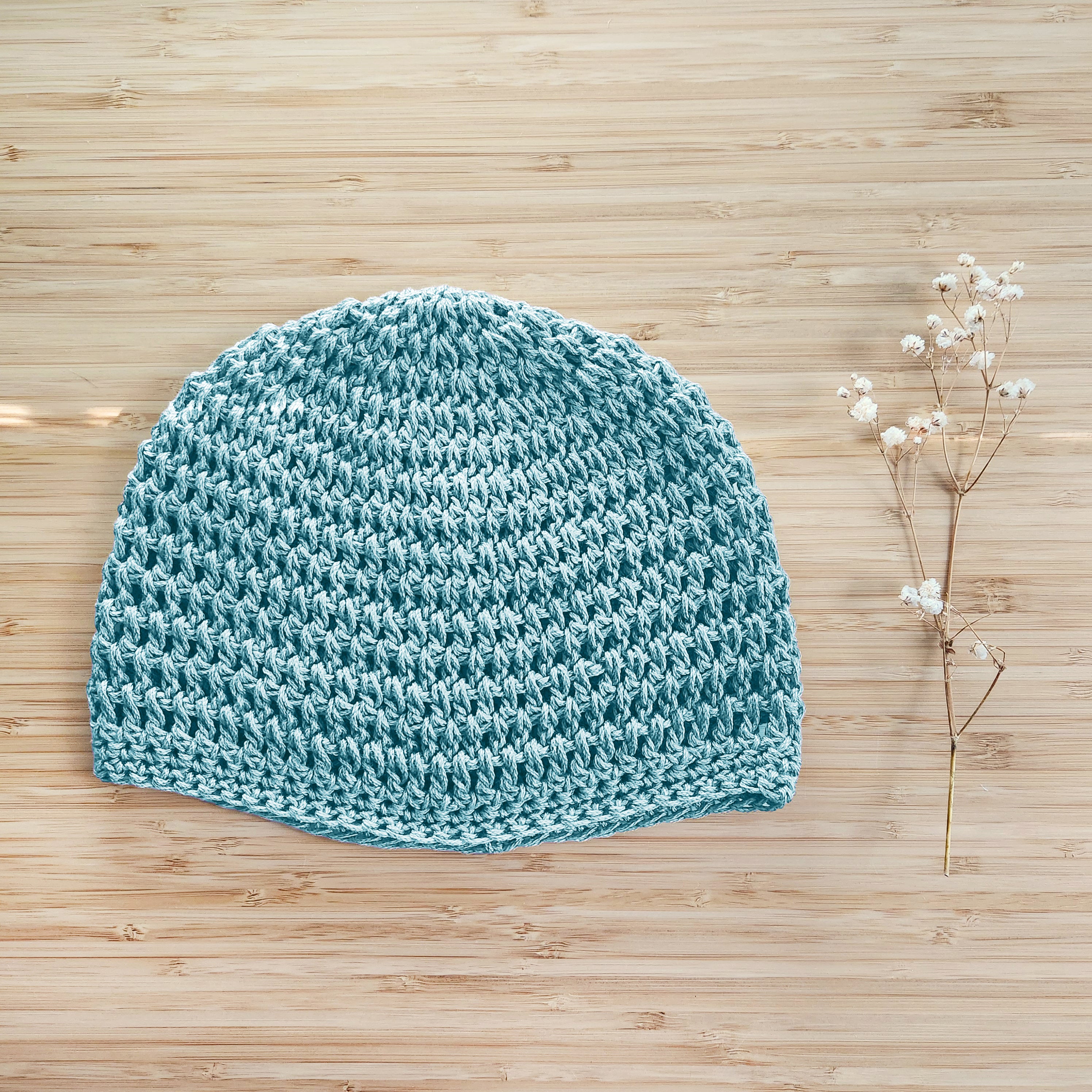 Light blue knitted beanie on a wooden surface with a small branch of flowers.