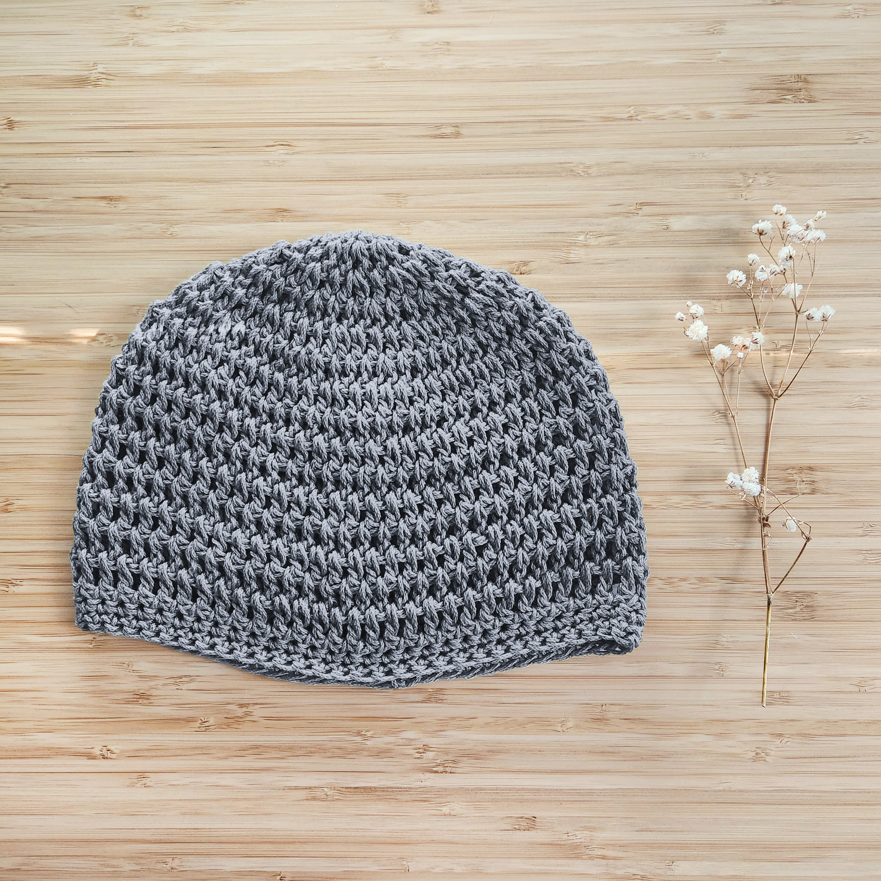 Gray knitted beanie on a wooden surface with a small branch of flowers.
