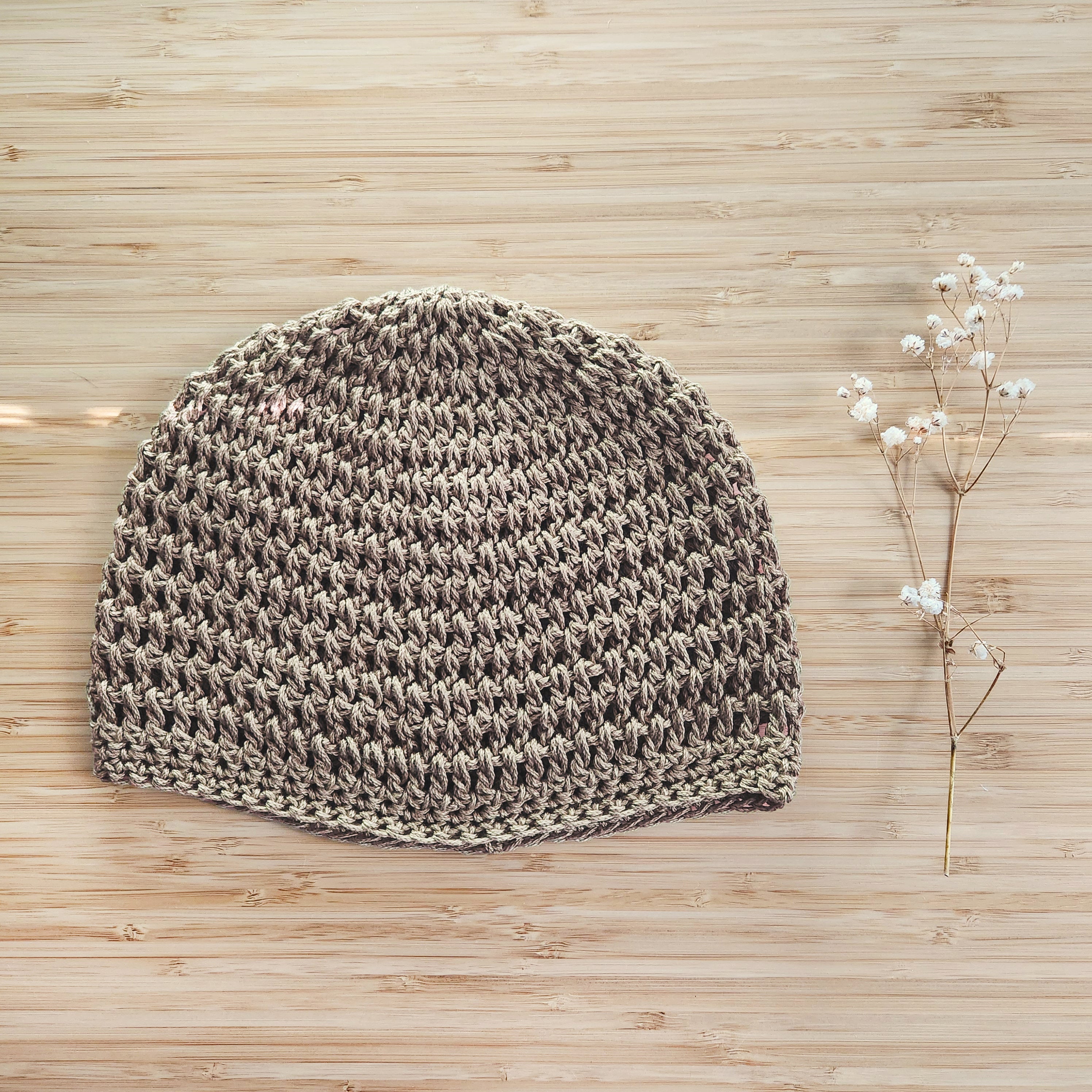 Light brown knitted beanie on a wooden surface with dried flowers.