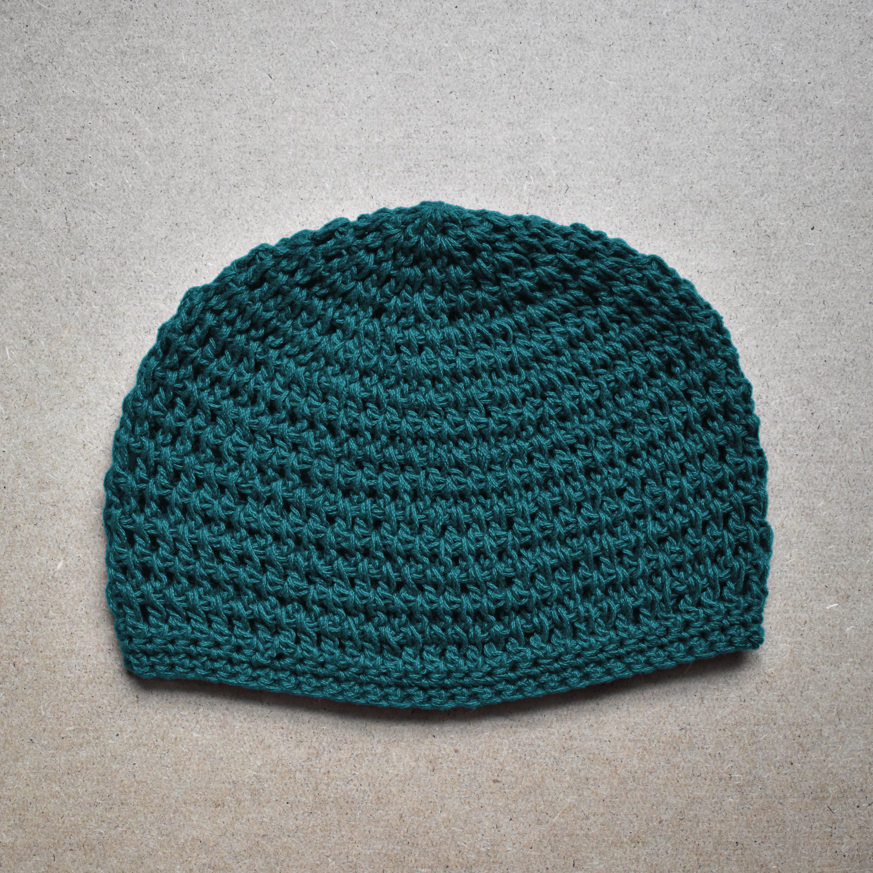 Teal knitted beanie on a gray background.