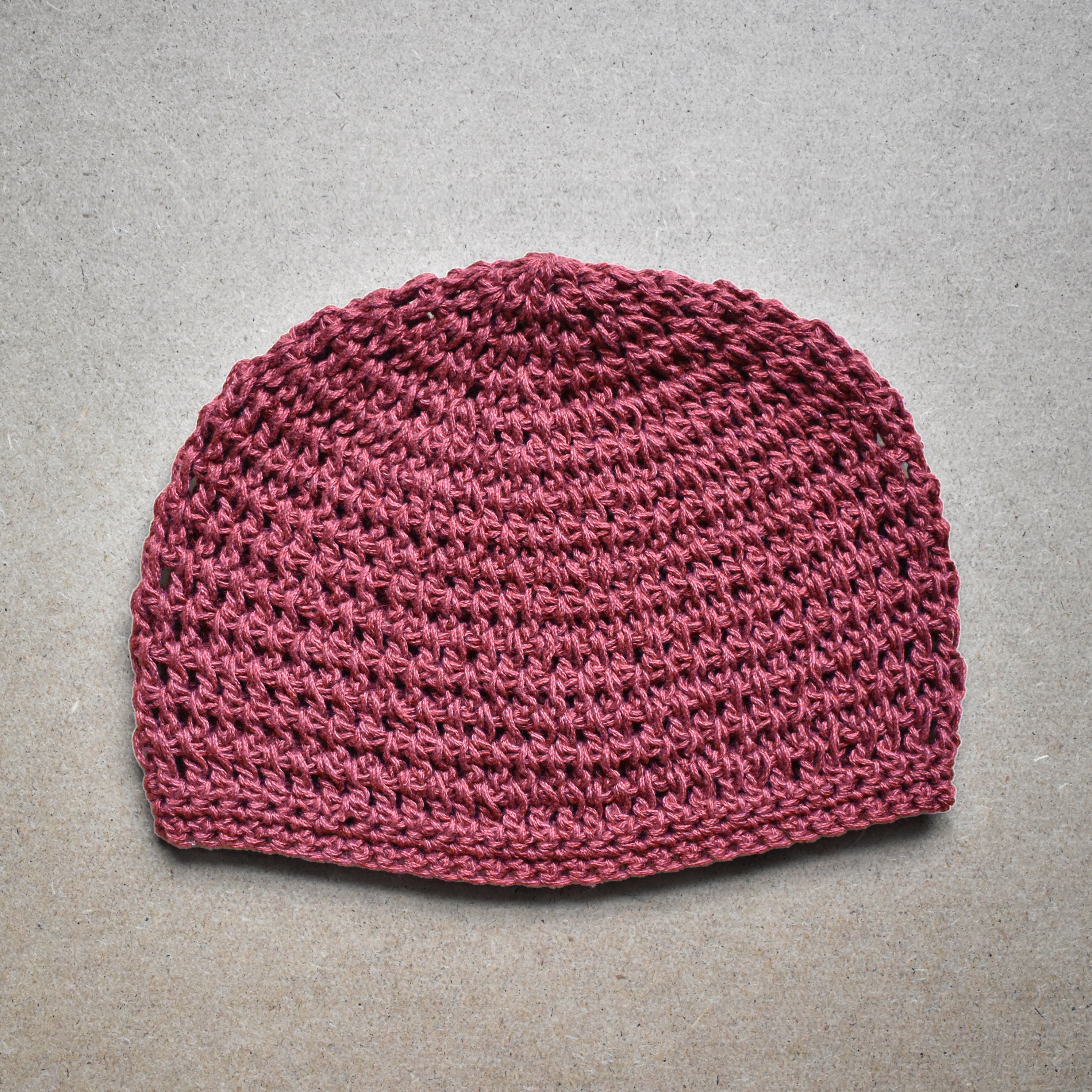 Terracotta pink knitted beanie on a gray background.