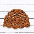 Amber brown crocheted lace cap on a white wooden surface.