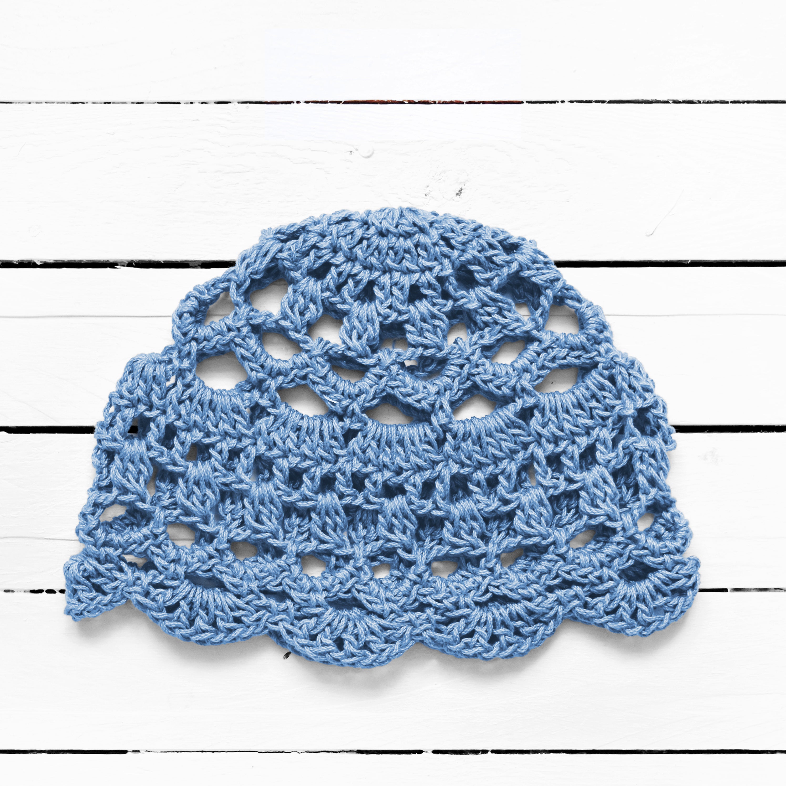 Baby blue crocheted boho lace cap on a white wooden surface.