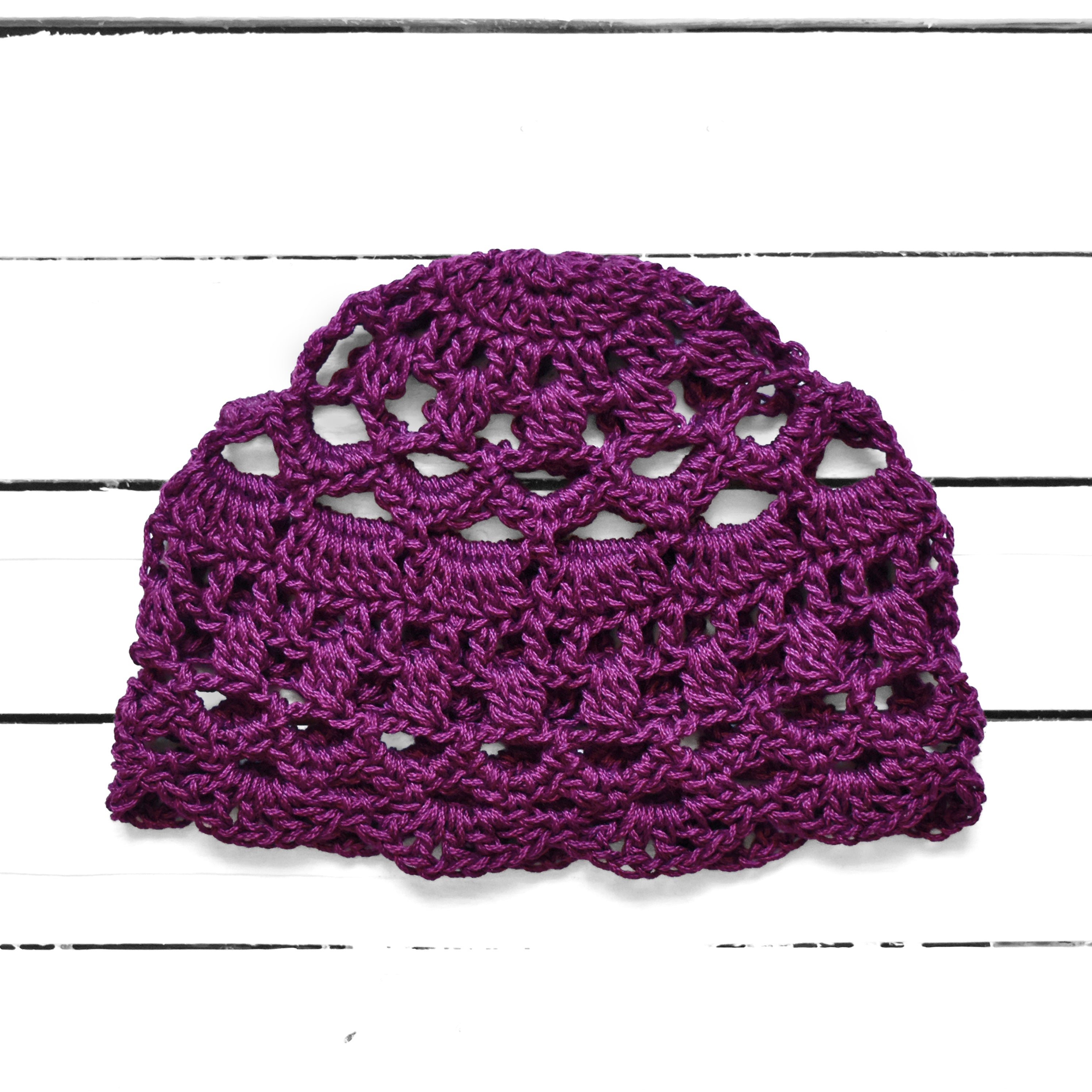 Dark purple crocheted summer cap on a white wooden background.
