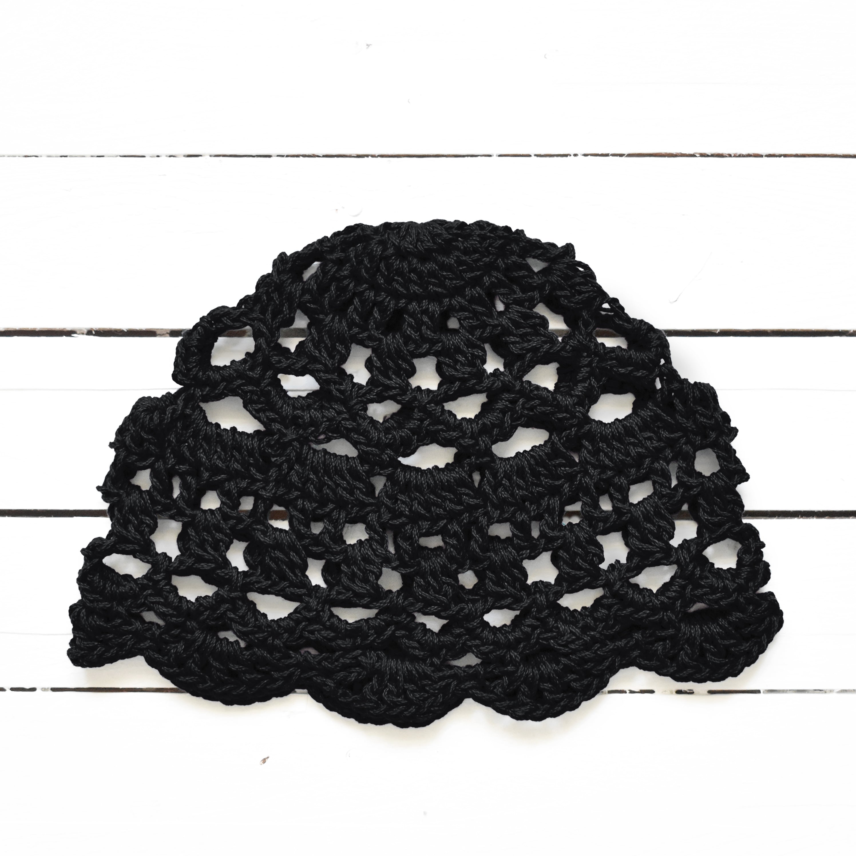 Black lace crochet hat on a white wooden surface.