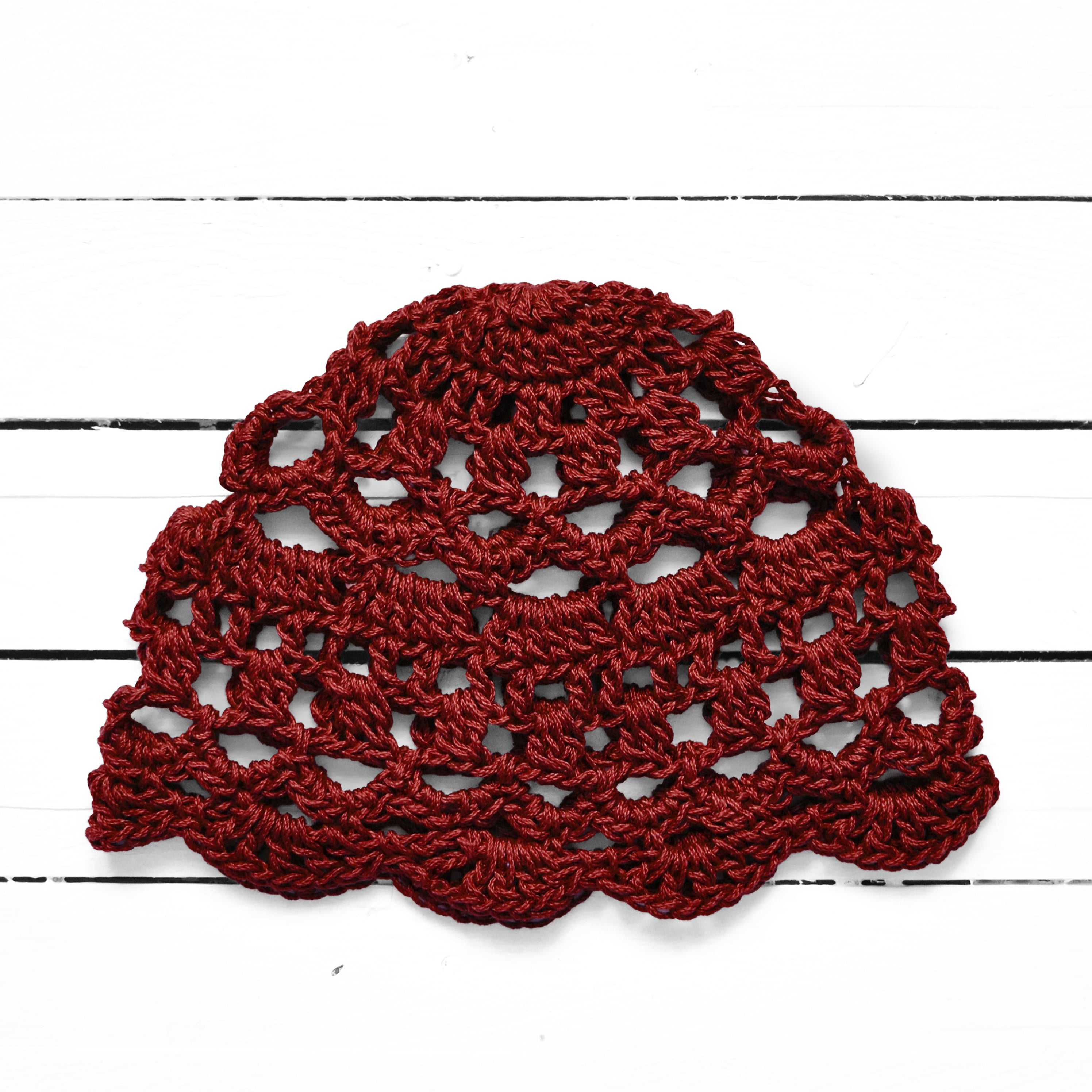 Burgundy red crocheted hat on a white wooden surface.