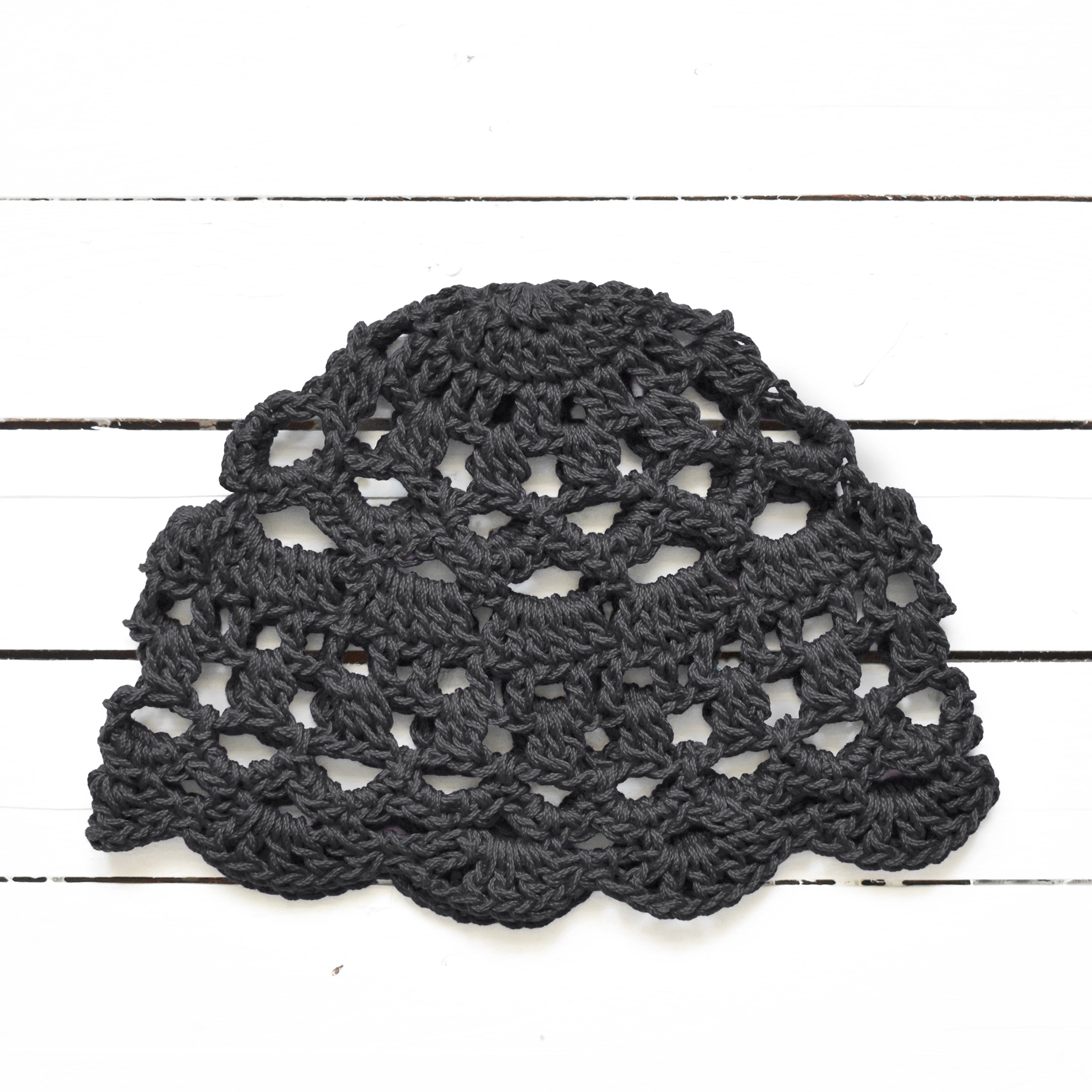 Dark gray crocheted lace cap on a white wooden surface.