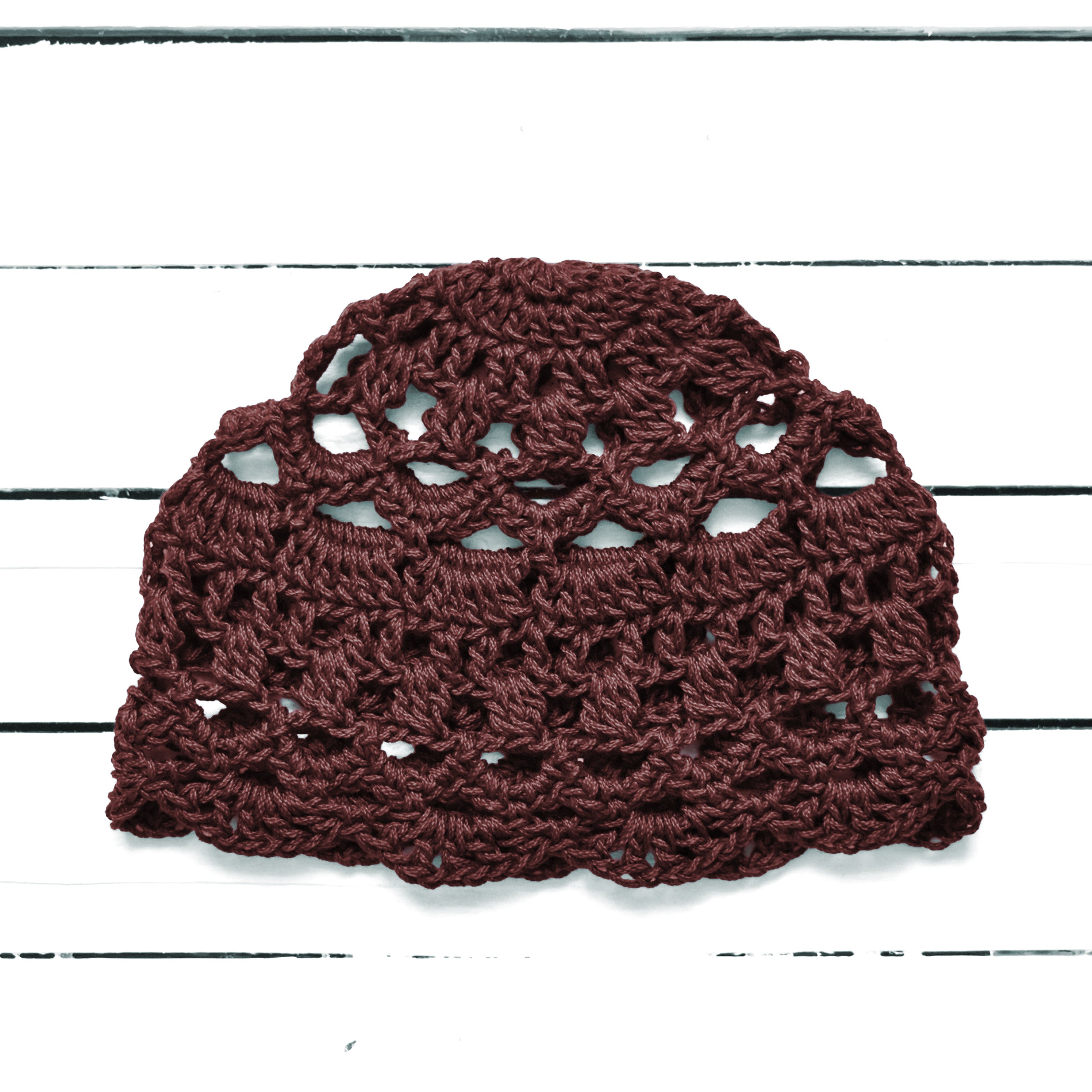 Brown crochet lace summer skullcap on a white wooden surface.