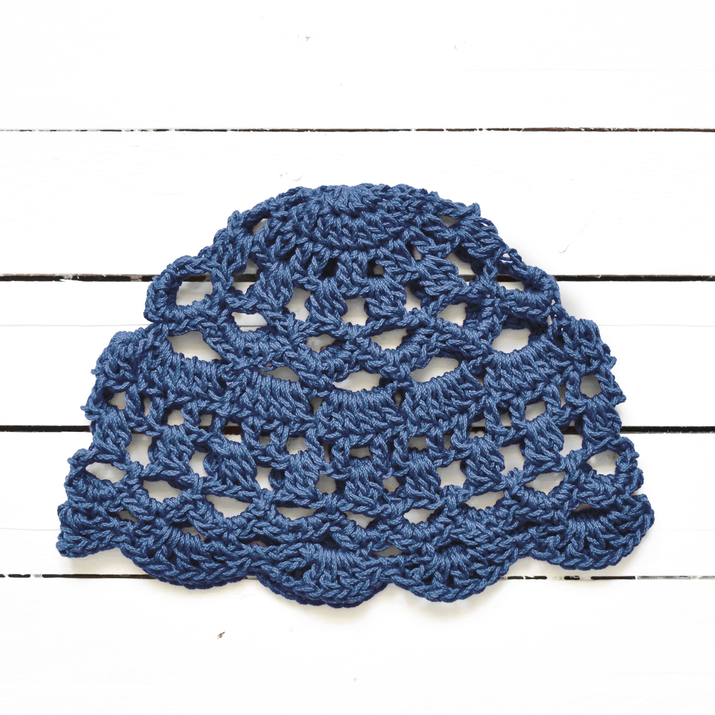 Gray-blue crocheted lace. hat on a white wooden surface