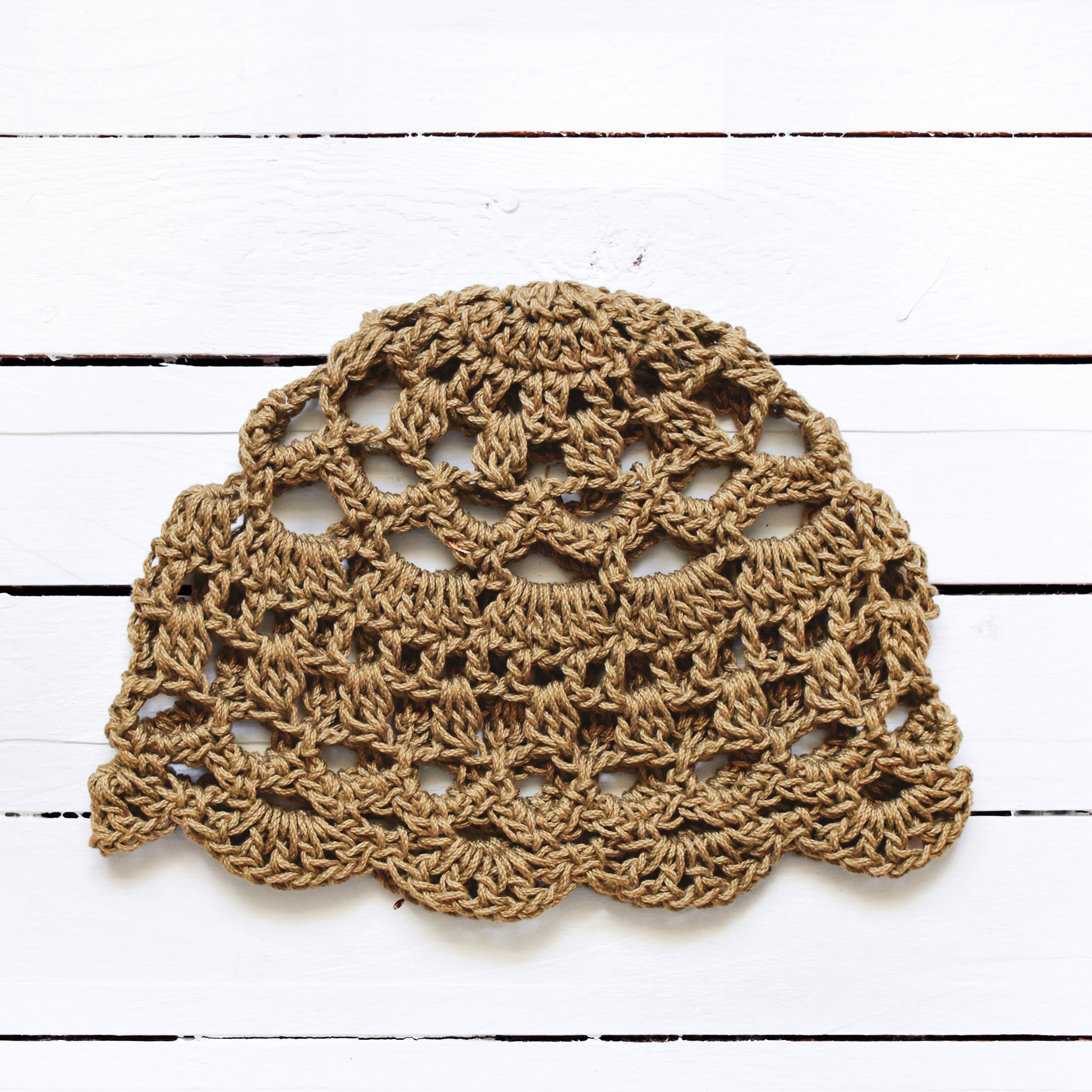 Light brown crocheted boho lace cap on a white wooden surface.