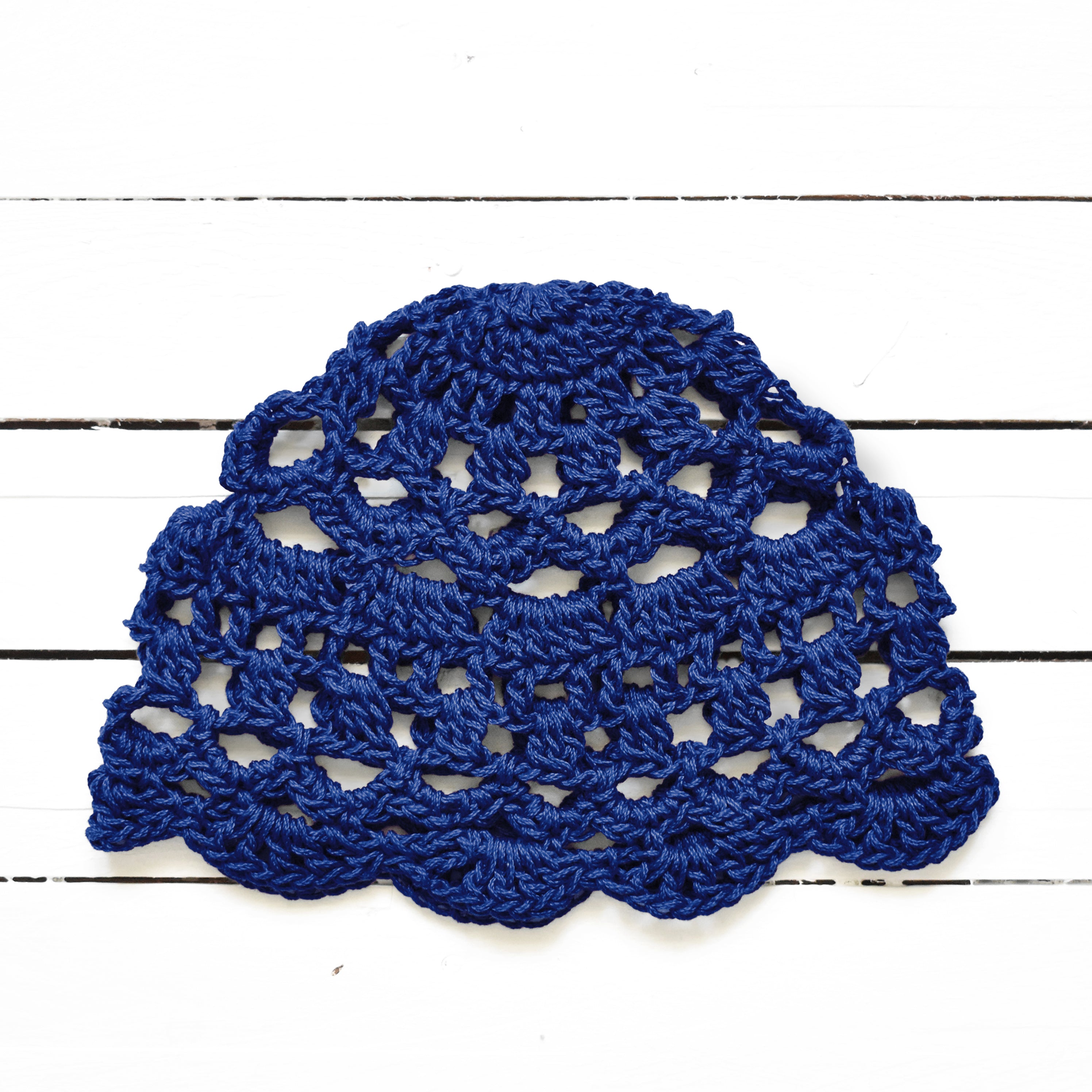 Indigo blue crocheted lace cap on a white wooden surface.