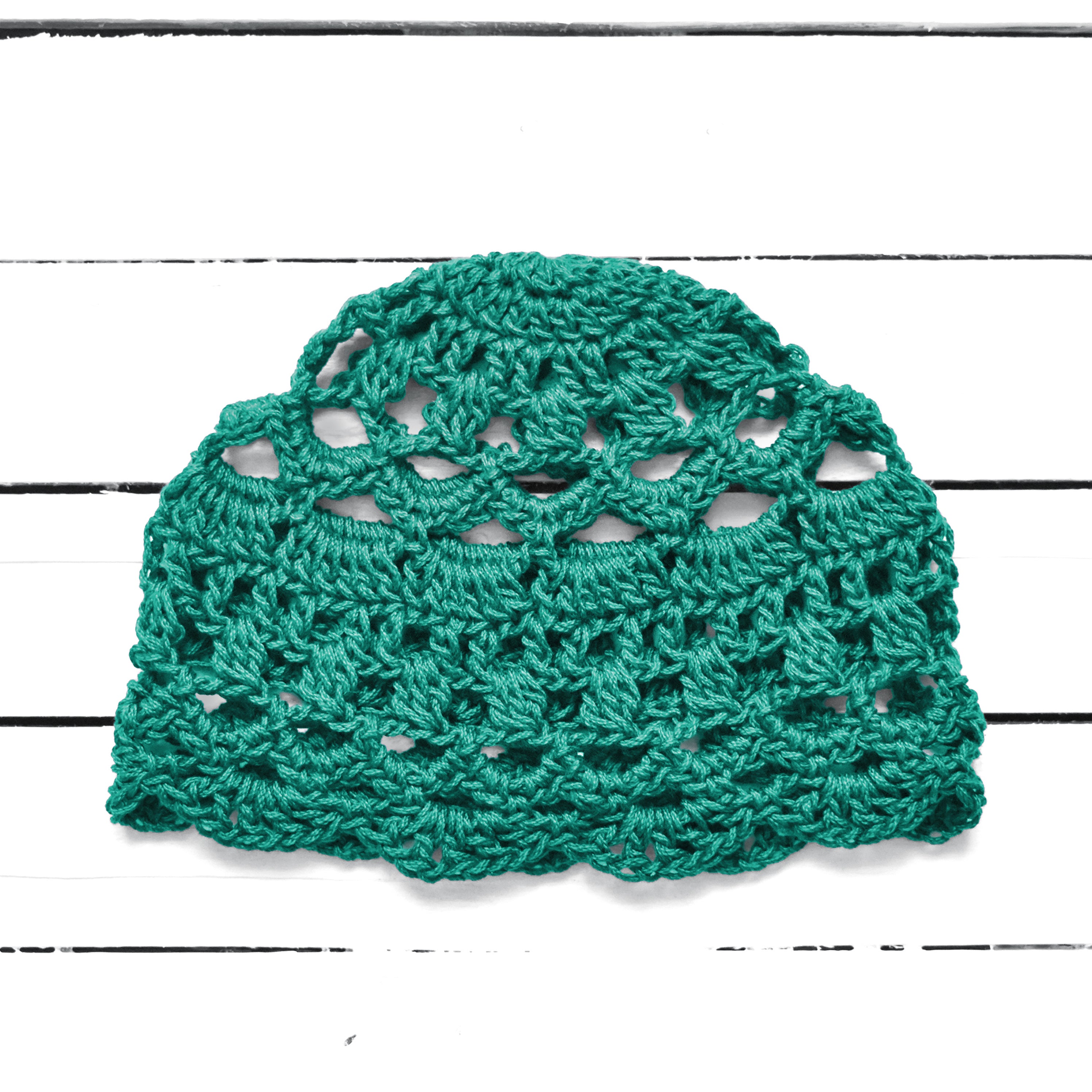 Light teal crocheted lace summer hat on a white wooden background.