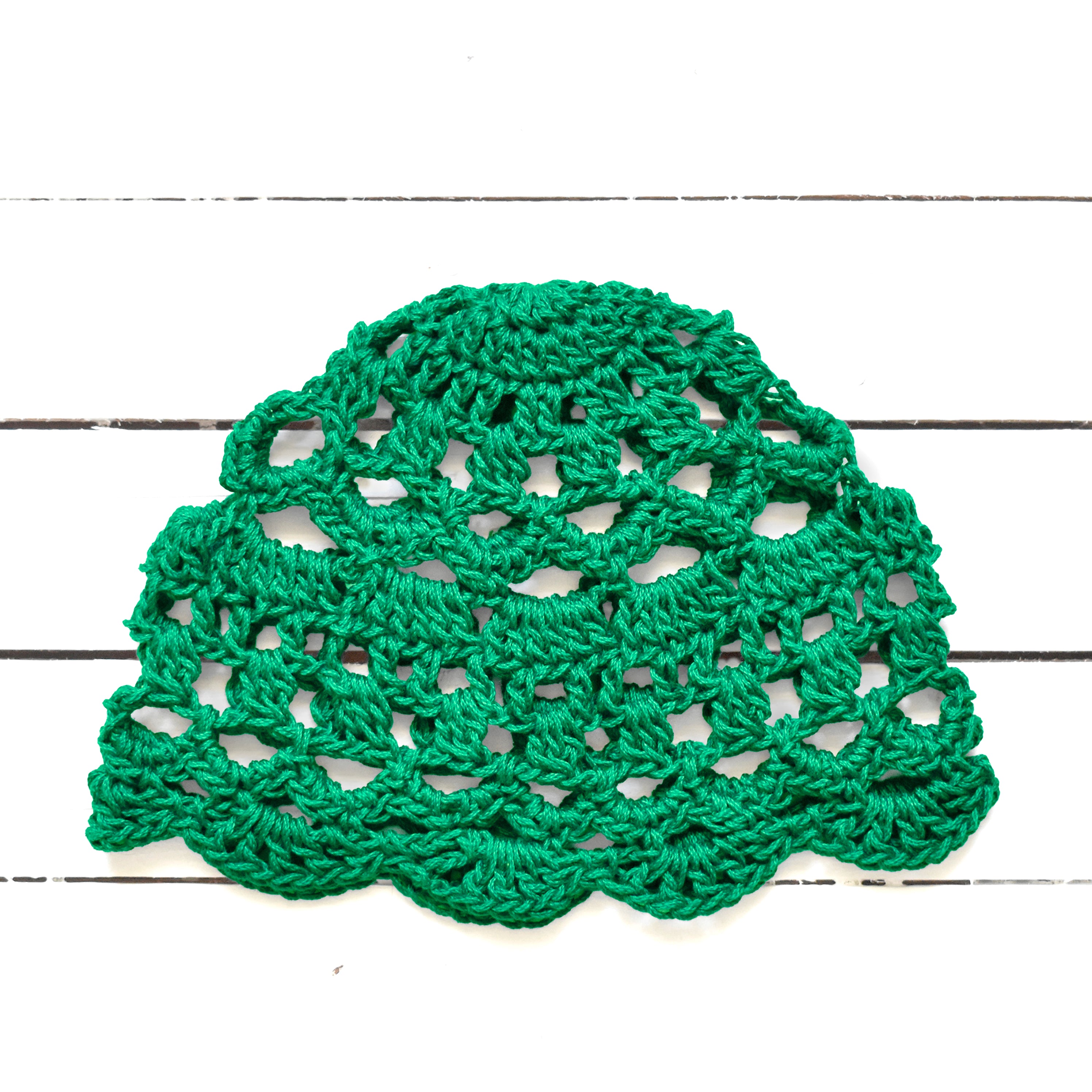 Green crocheted bohemian lace skull cap on a white wooden surface.