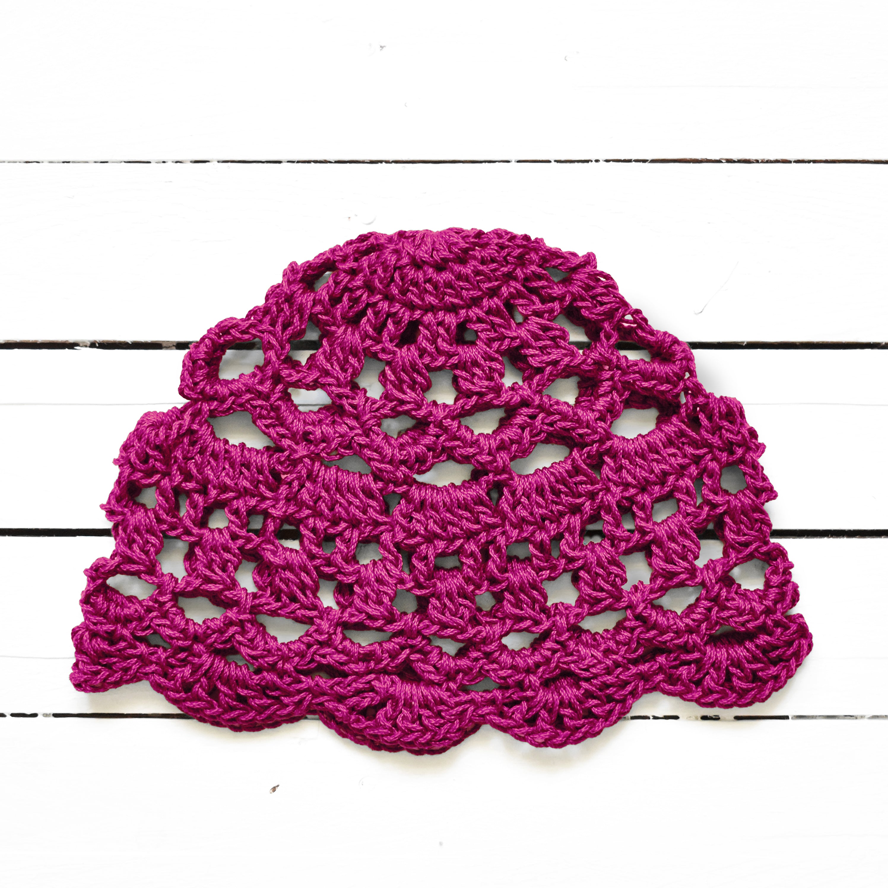 Bright pink crocheted lace cap on a white wooden surface.